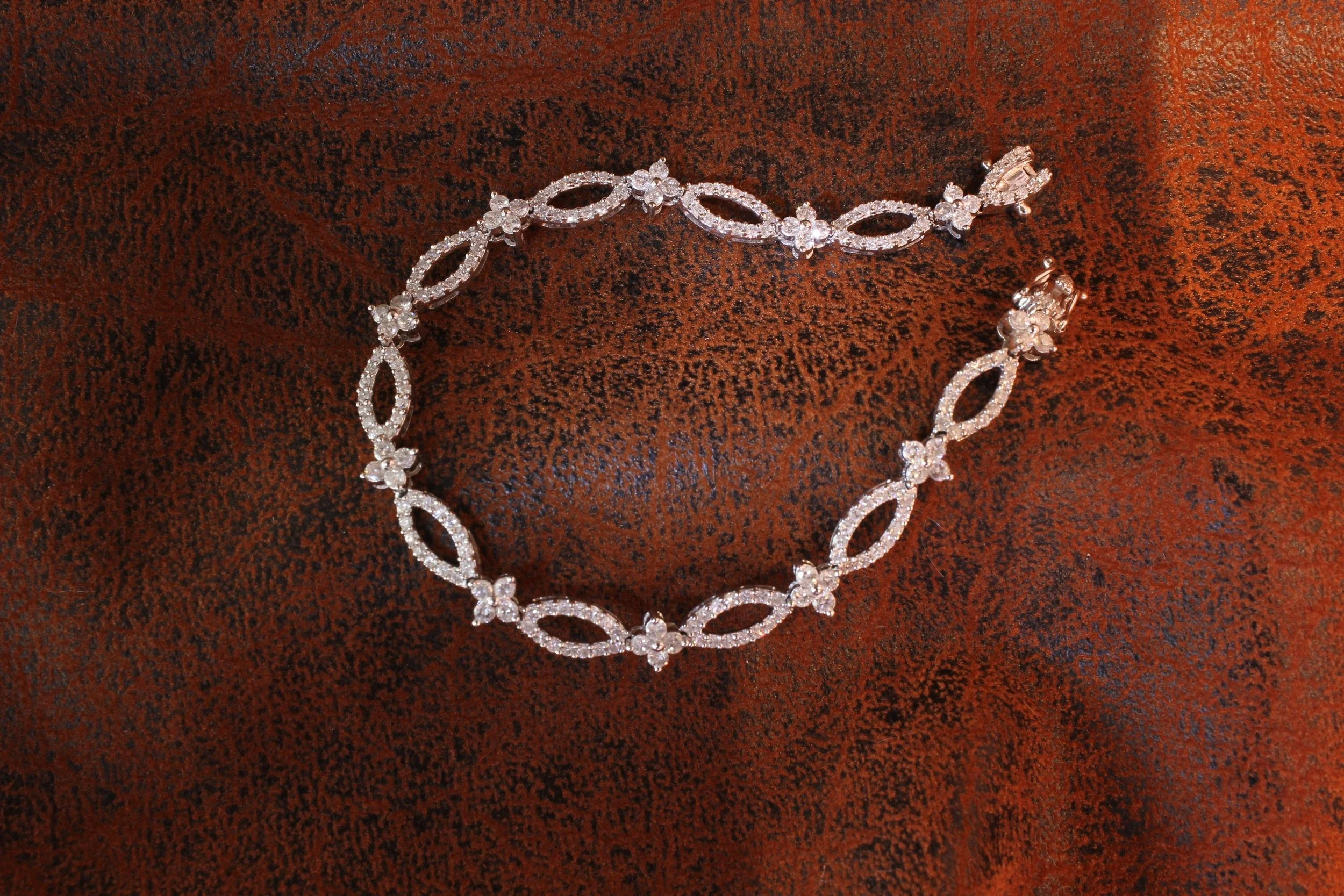 A silver and crystal necklace with floral and oval-shaped links, laid on a reddish-brown textured surface.