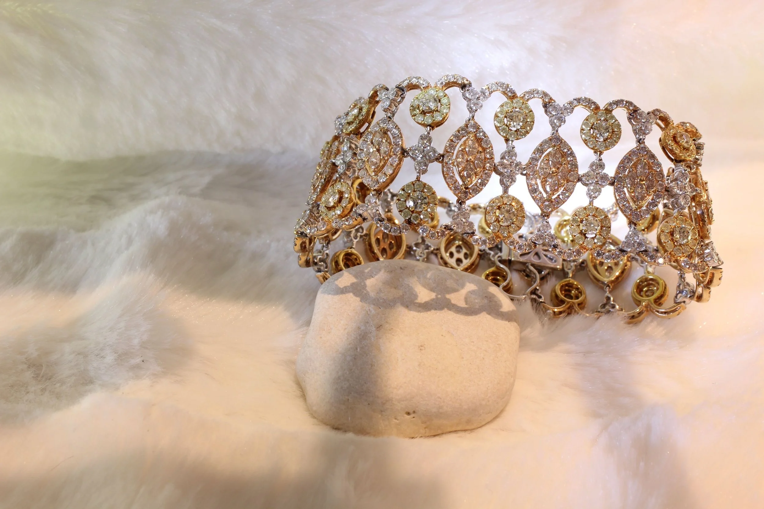Gold and white gold bracelet with diamond embellishments displayed on small white rocks, against a soft, textured light background.