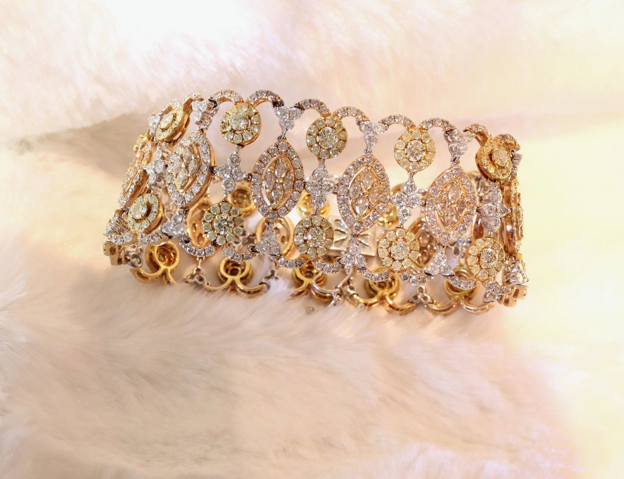 Close-up of elaborate gold and diamond jewelry consisting of rings and bracelets, displayed on a soft, pale background.