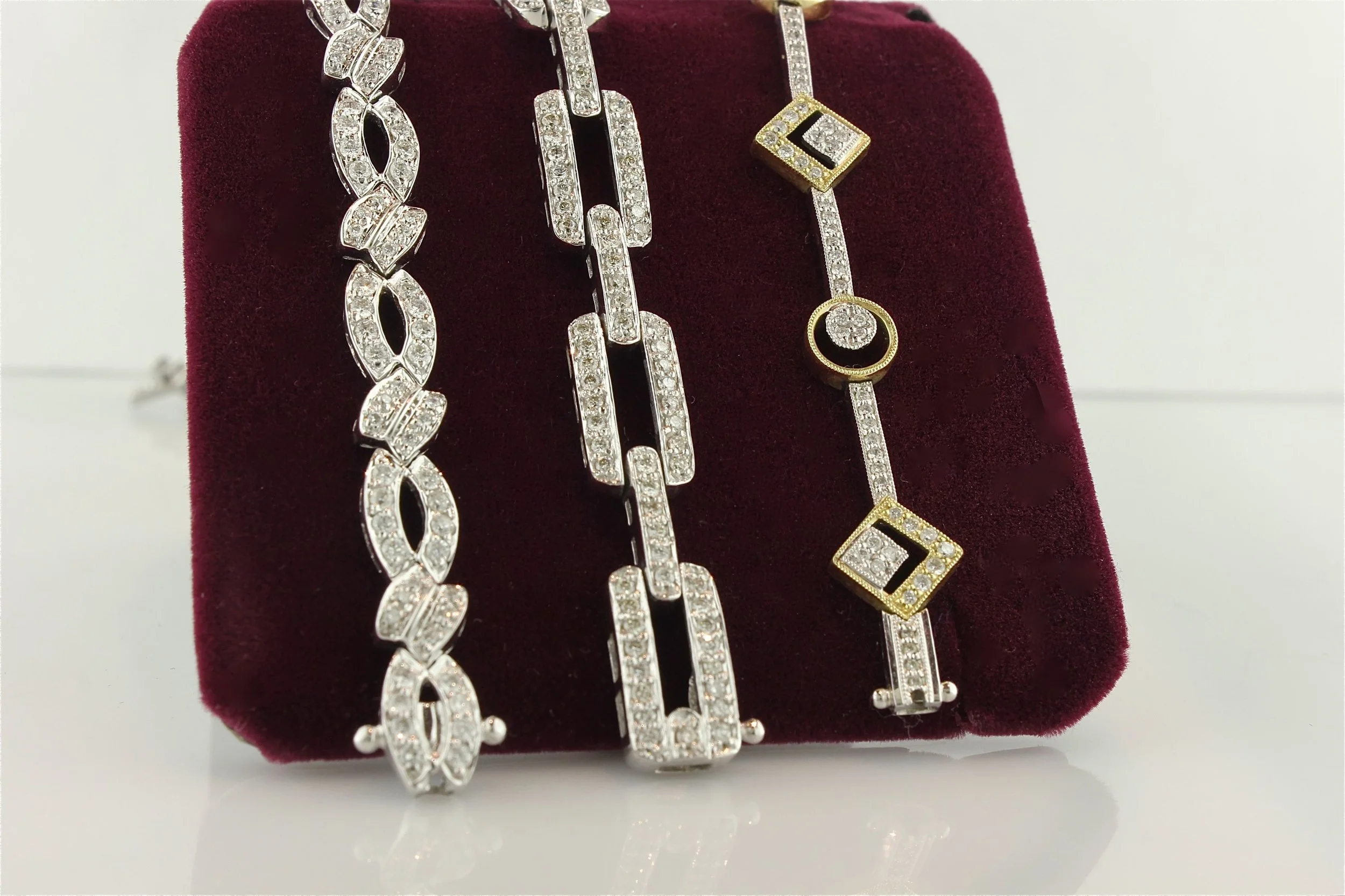 Three diamond-studded necklaces hanging on a burgundy display stand.