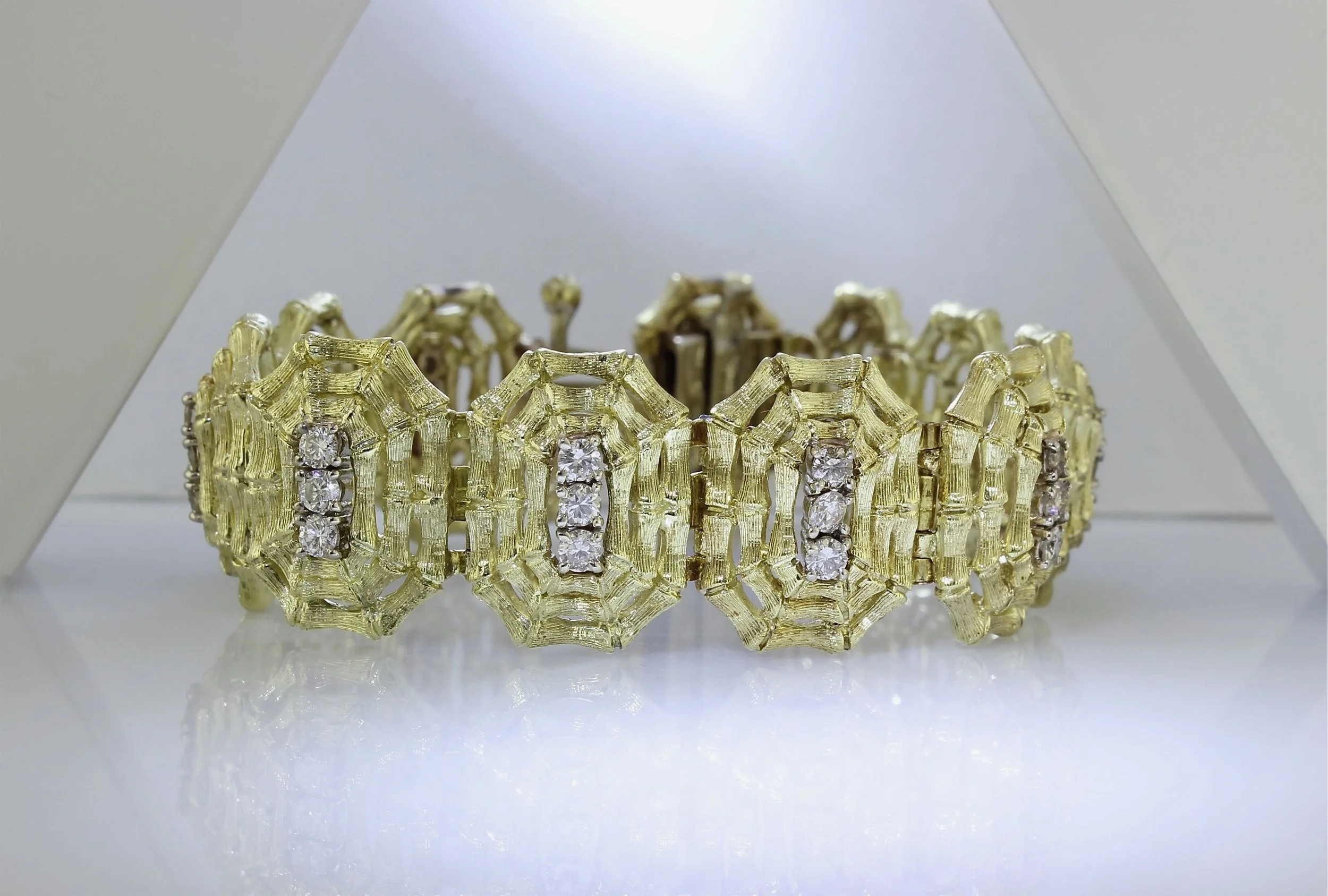 A gold bracelet adorned with multiple diamonds, displayed inside a white box with the lid open.
