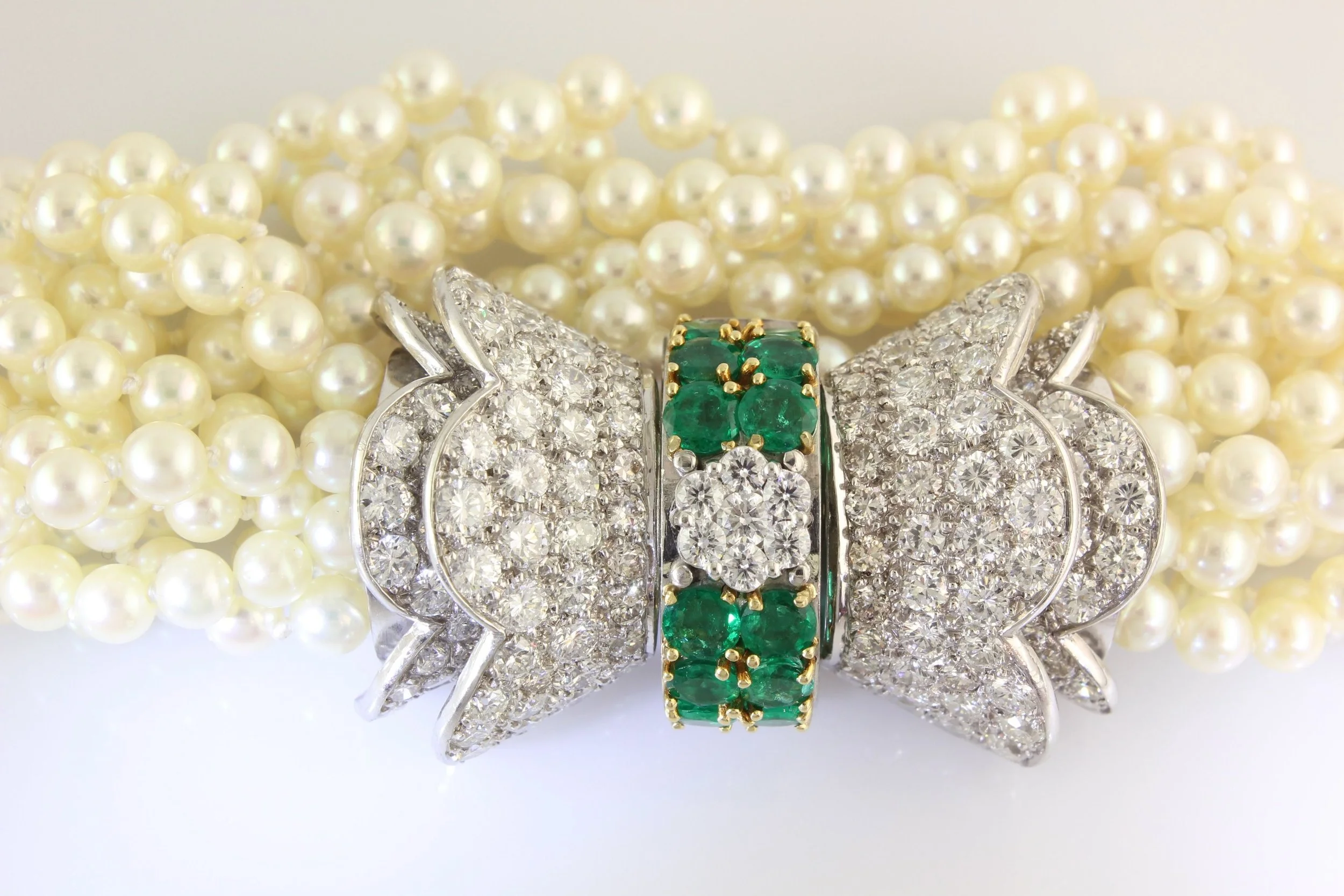 Close-up of pearl necklaces and diamond-encrusted jewelry with emerald accents.