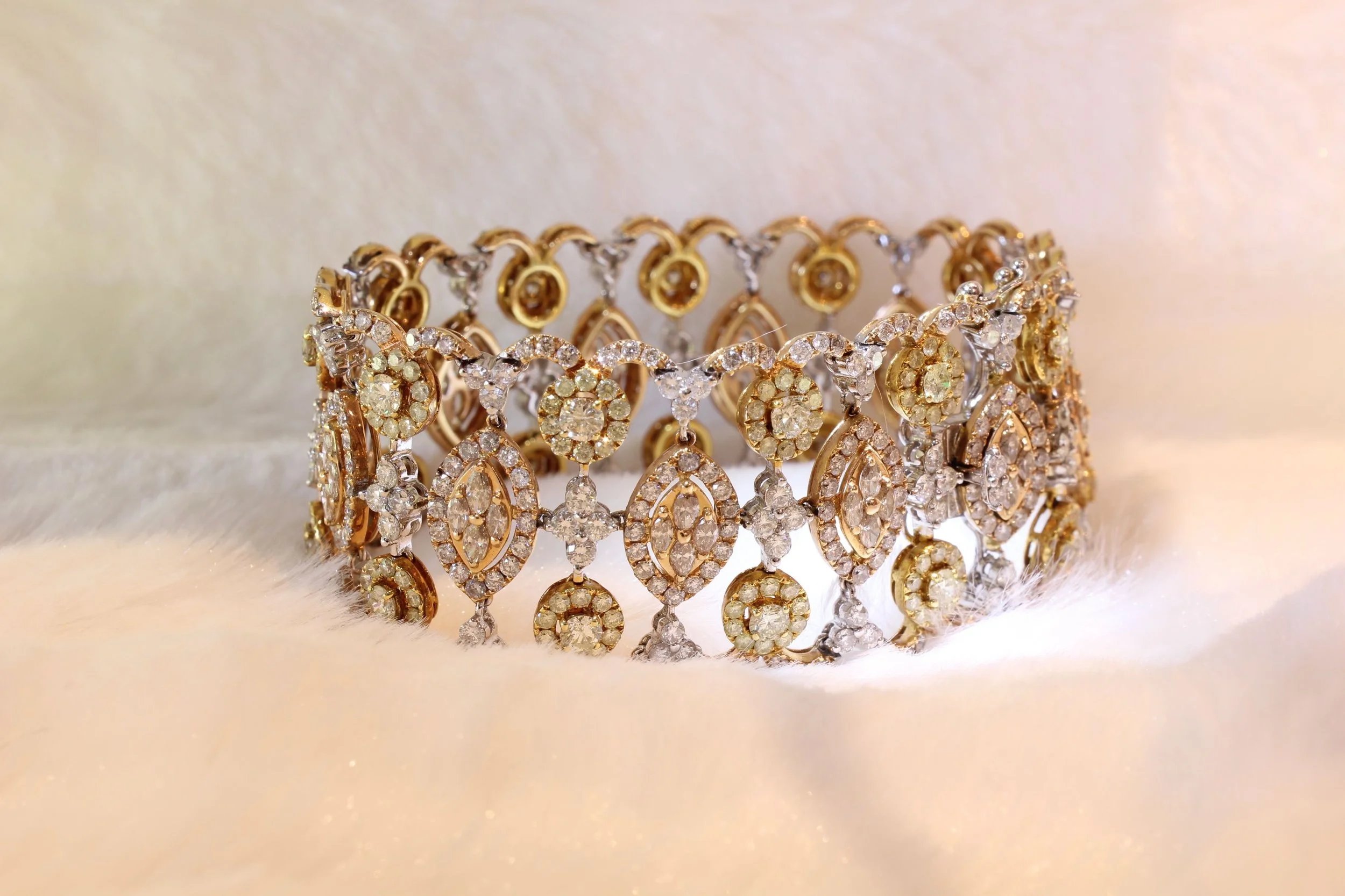 Gold and silver bracelet adorned with numerous small, sparkling diamonds, resting on a soft, white textured surface.