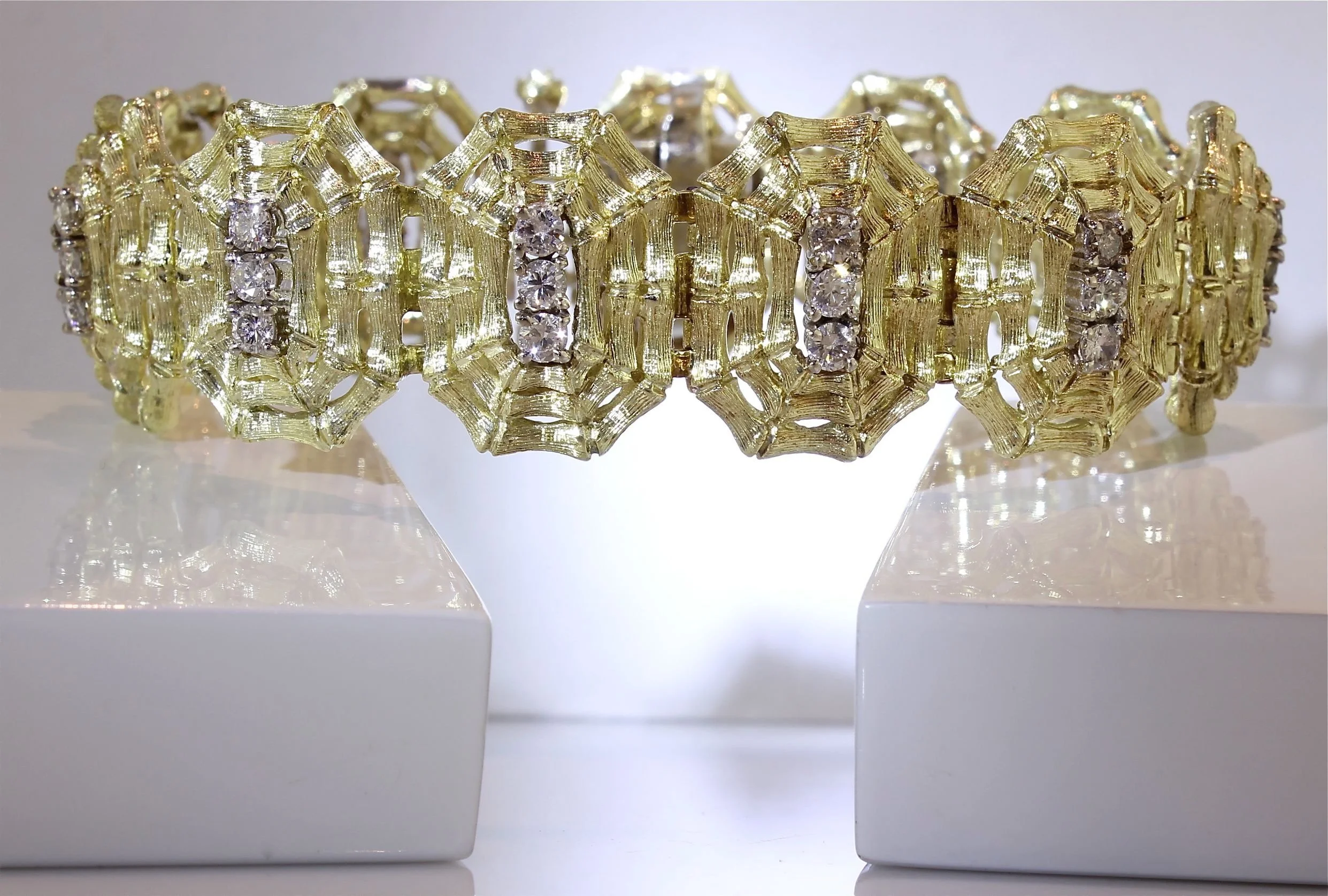 Close-up of a gold bracelet with diamond accents, resting on a white display stand.