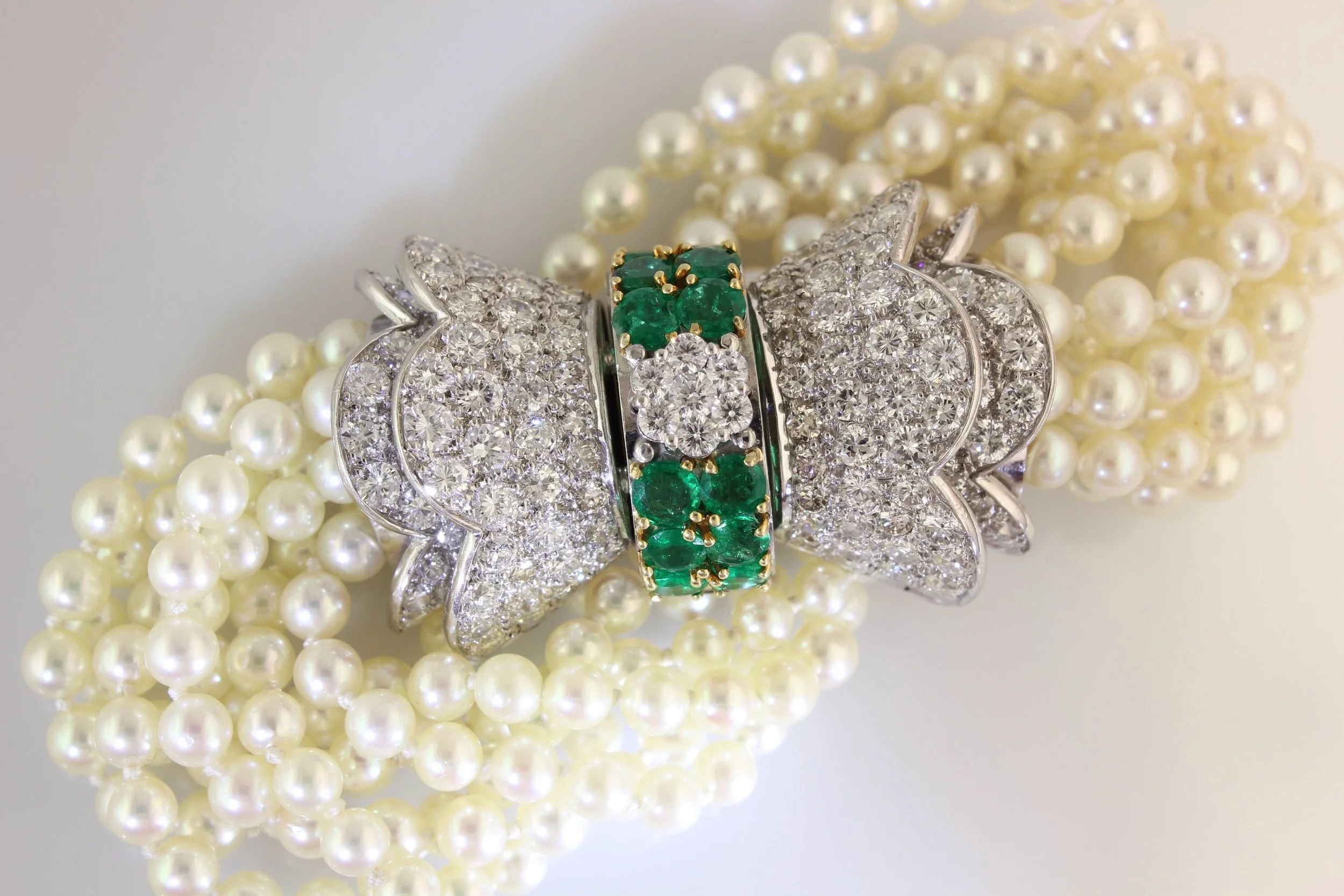 A close-up of a pearl necklace with a diamond and emerald butterfly-shaped brooch placed on it.