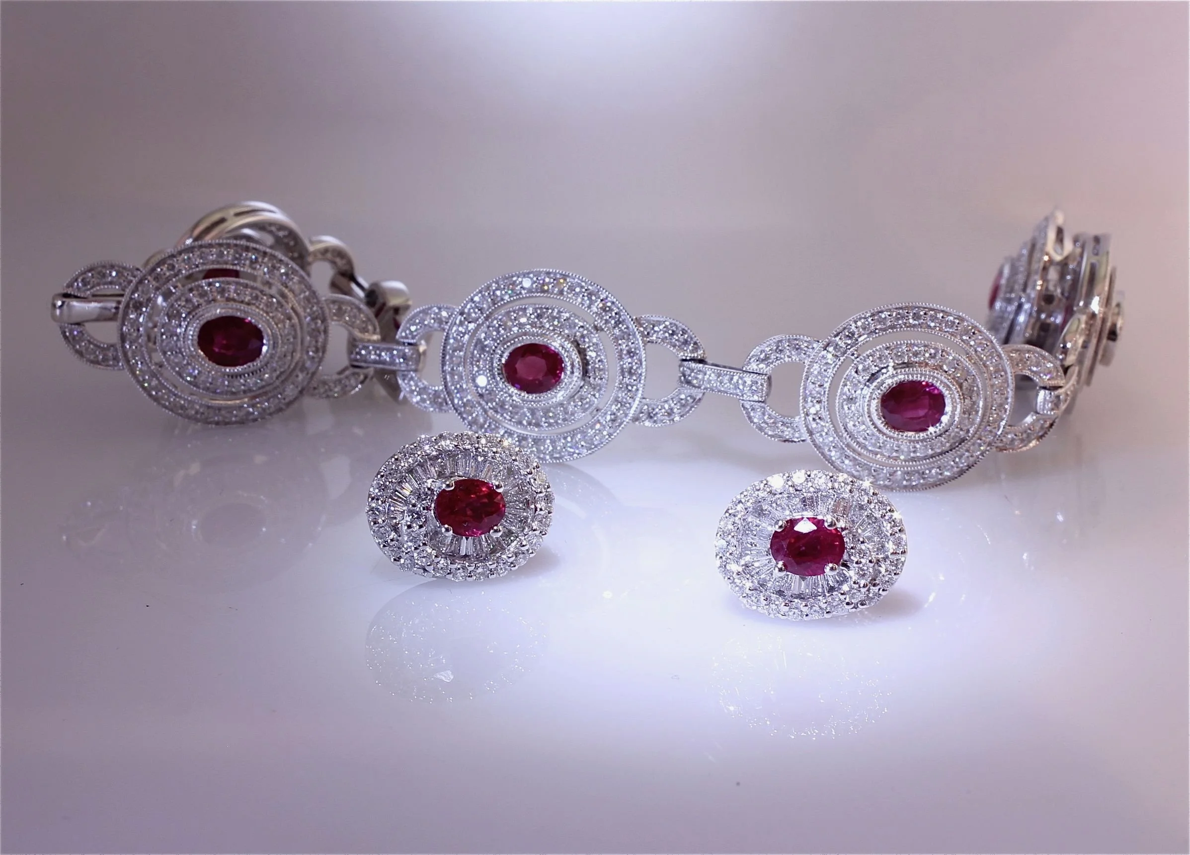 A silver bracelet with multiple round settings, each featuring a central red gemstone surrounded by small clear stones, and matching earrings with the same design.