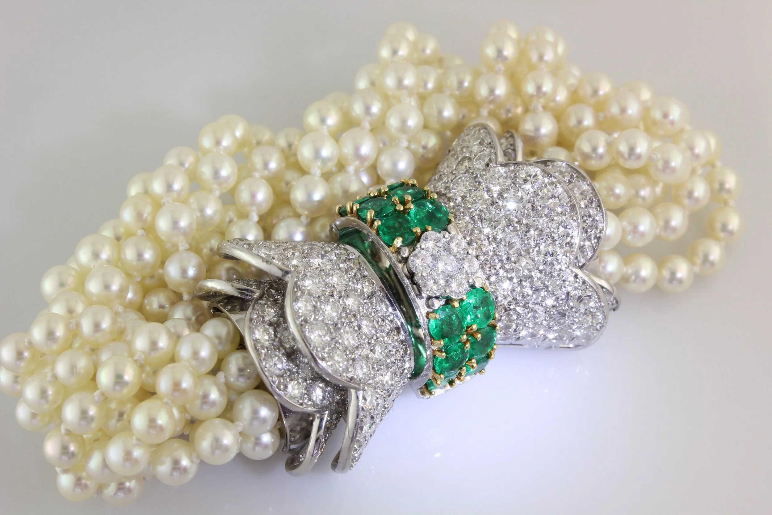 Close-up of a pearl necklace and several pieces of diamond and emerald jewelry including rings and a brooch.