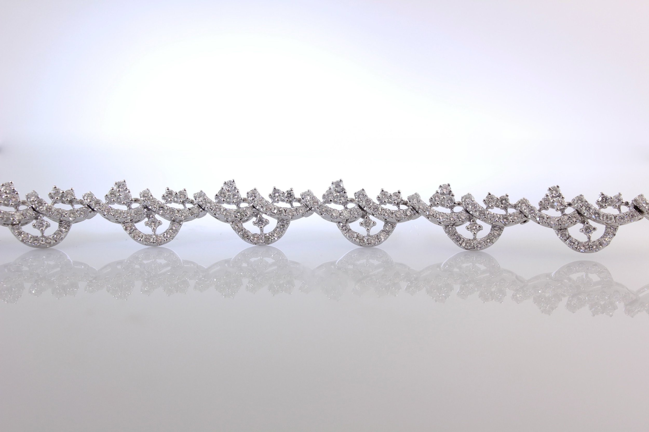 Close-up of a sparkling diamond bracelet with intricate design, reflected on a smooth, reflective surface.
