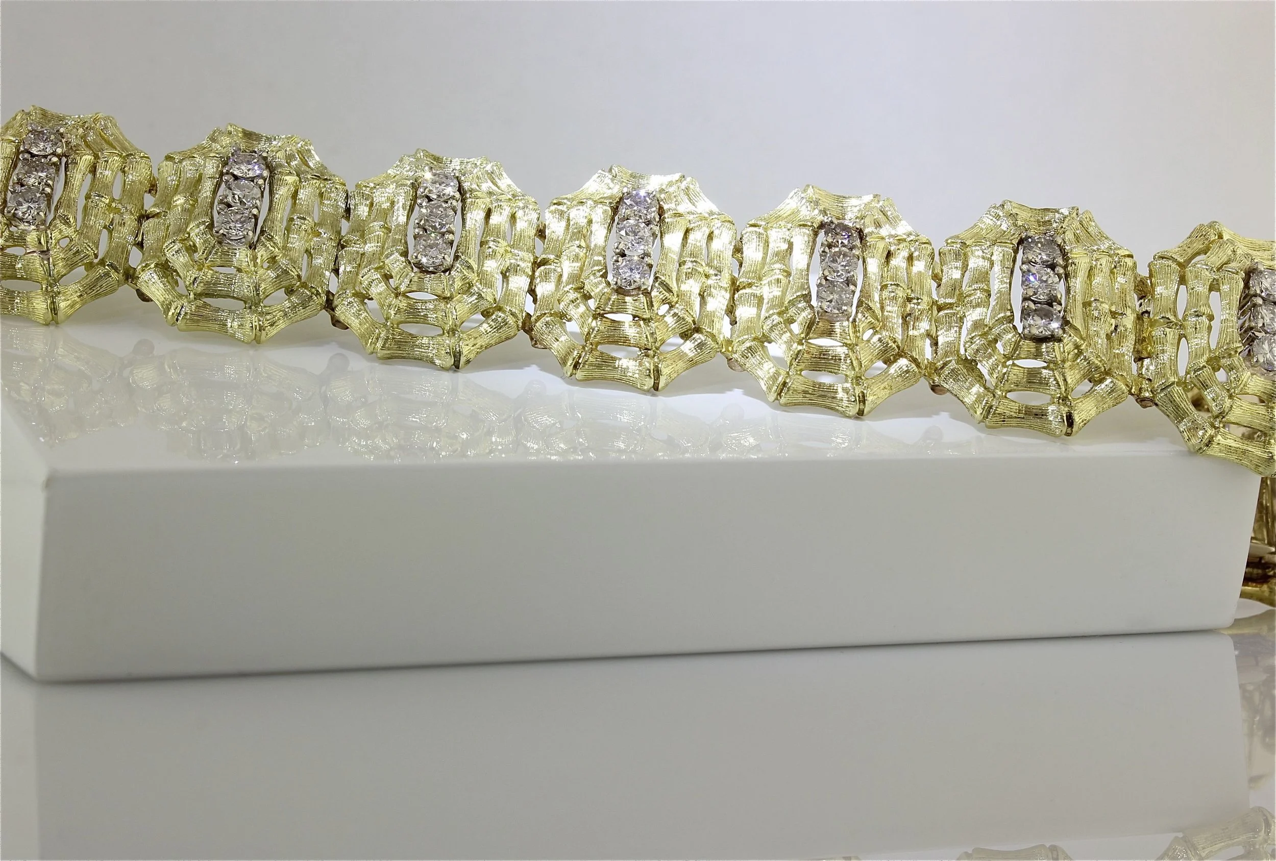 Gold jewelry bracelet with diamond accents on a white display stand.