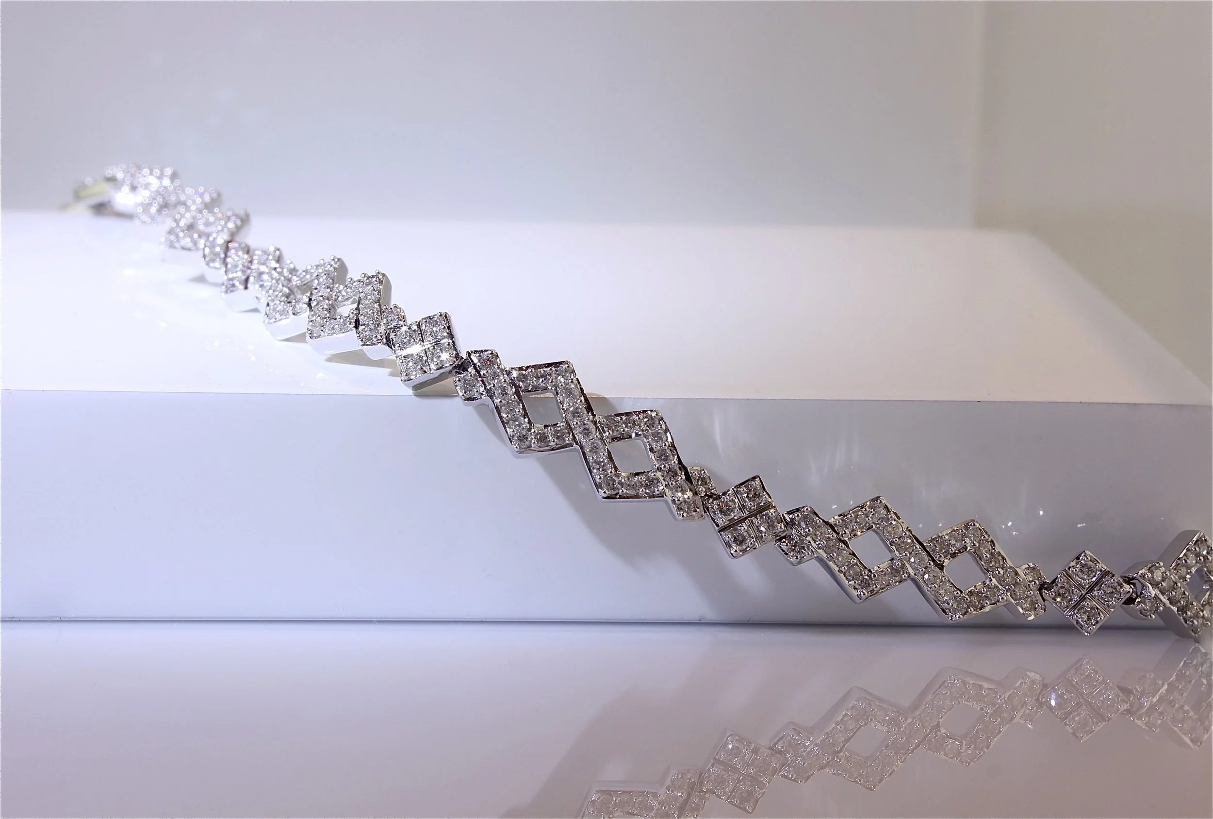 A gold bracelet encrusted with small clear diamonds, displayed on a white surface with glass diamond-shaped beads nearby.