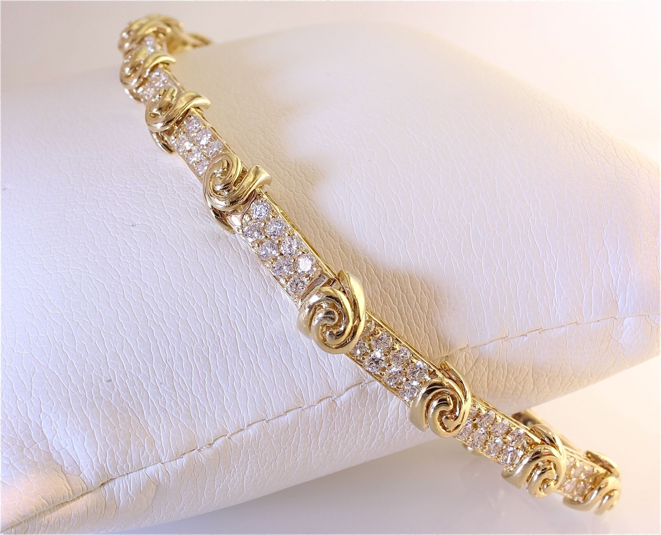 Close-up of a gold bracelet with intricate designs and embedded sparkling stones, resting on a textured light surface.