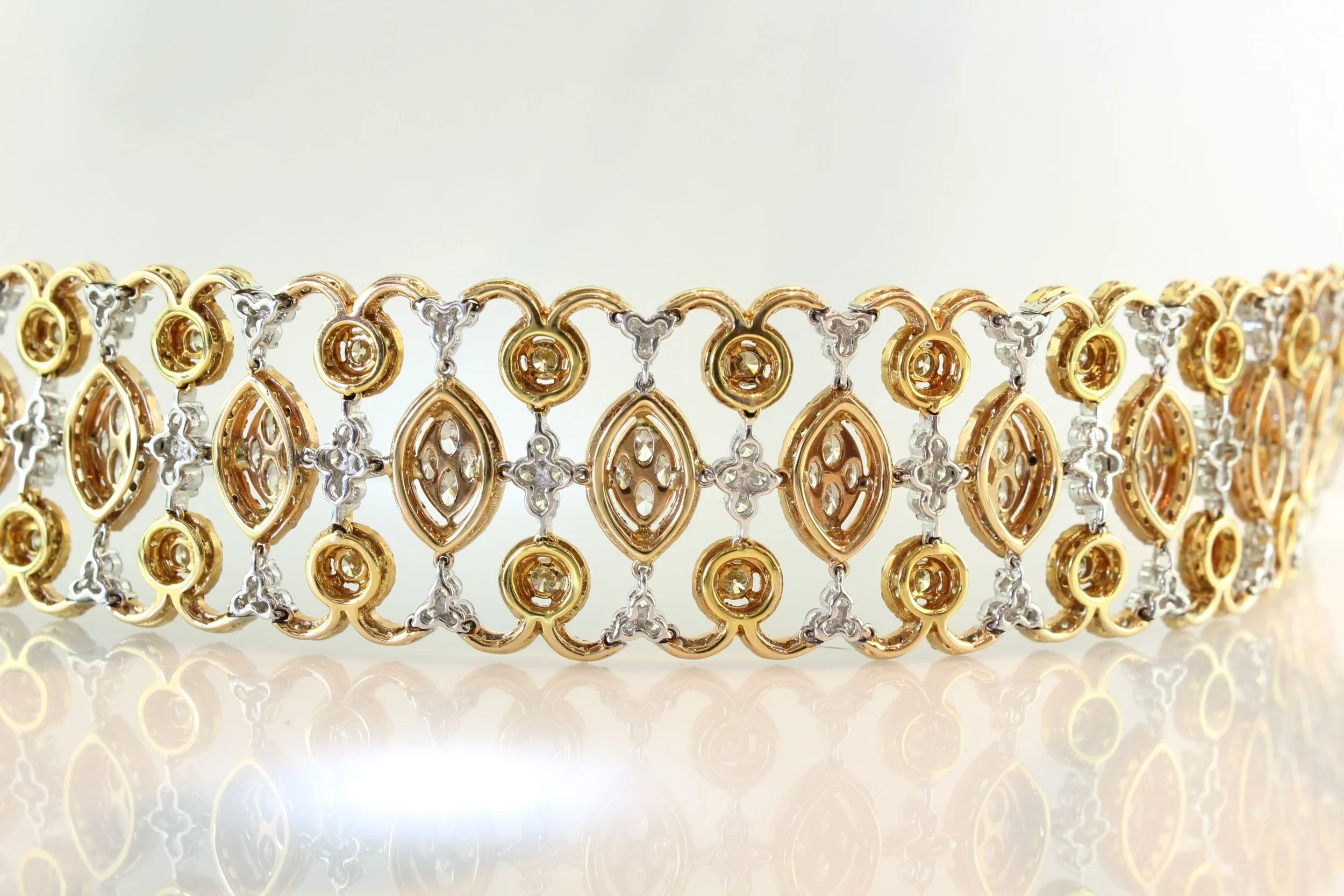 Close-up of a gold and silver jewelry bracelet with an ornate, interconnected pattern, against a white background.