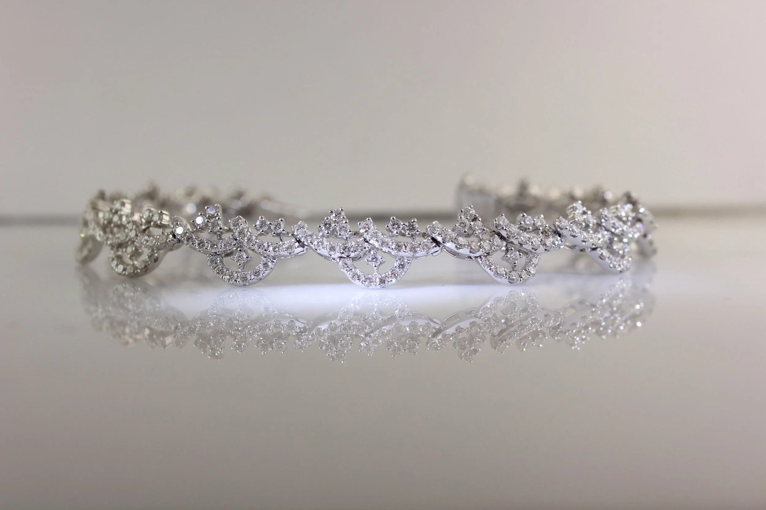A silver tiara encrusted with numerous clear gemstones, resting on a reflective surface, creating a mirror image.