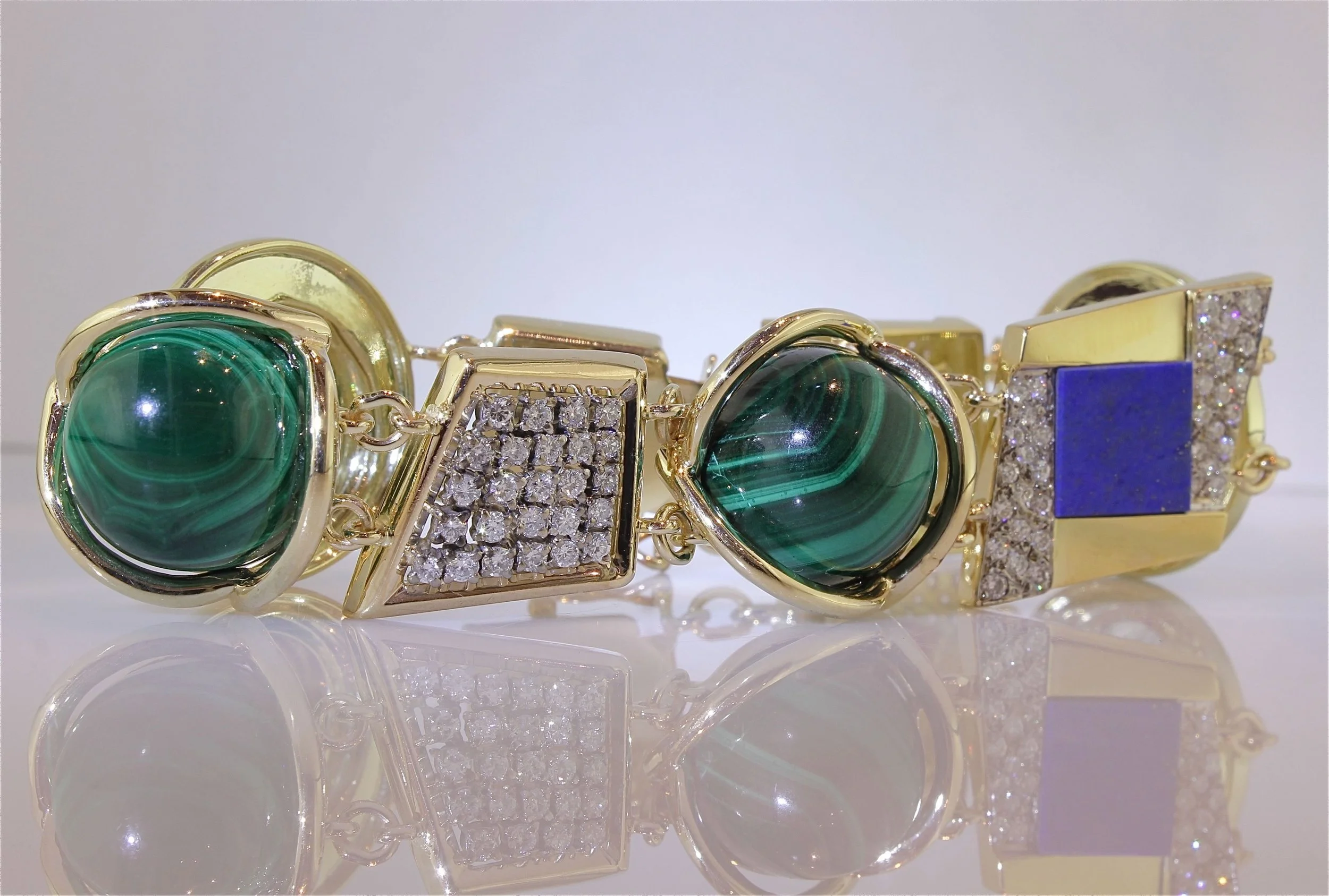 Close-up of a gold bracelet with large green malachite stones, adorned with clusters of small clear rhinestones, and a large blue rectangular stone.