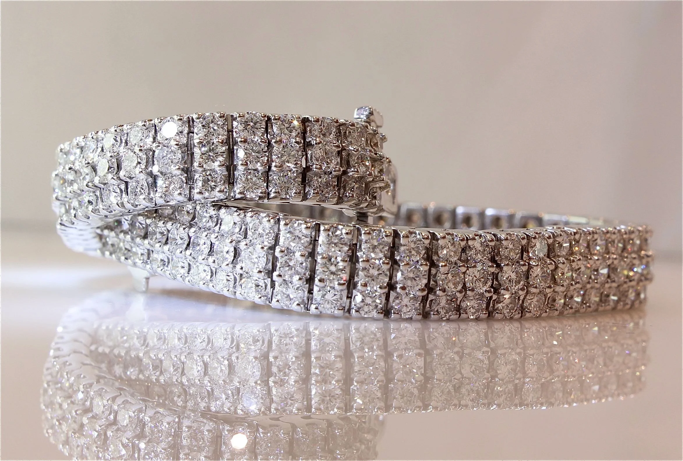 Close-up of a sparkling diamond tennis bracelet reflecting on a shiny surface against a soft background.