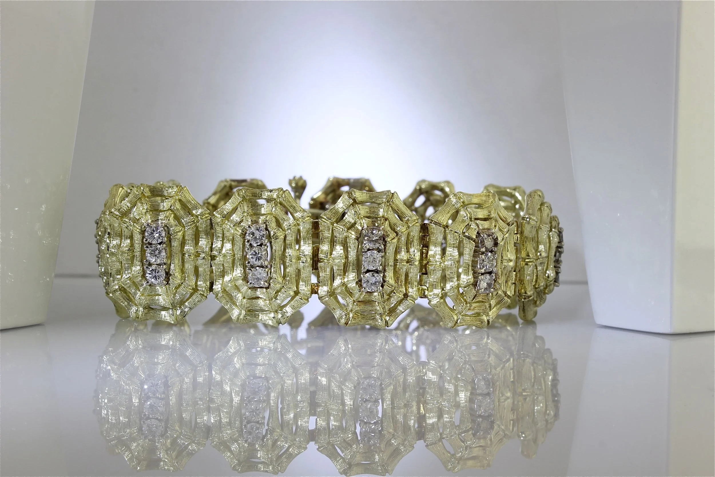 Close-up of a gold bracelet with a geometric design and embedded diamonds, reflected on a shiny surface.