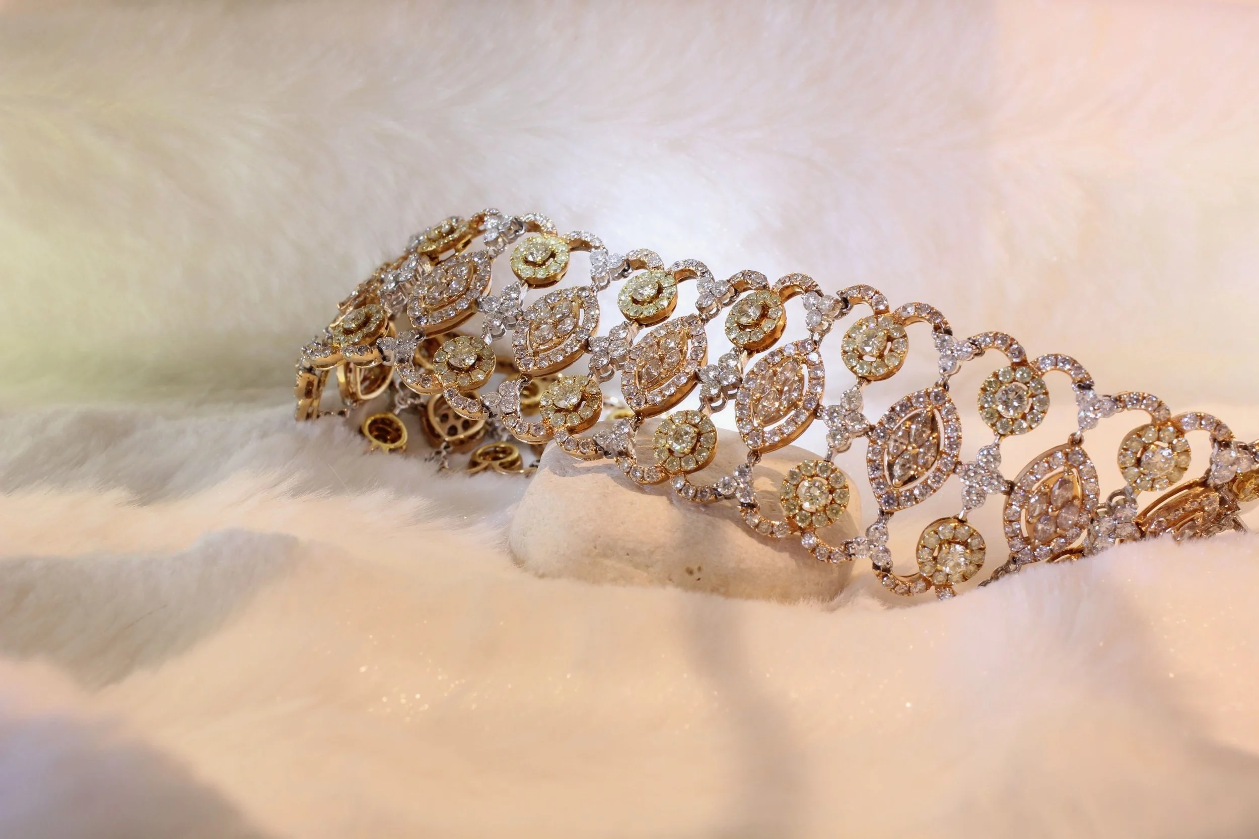 A close-up of gold and diamond jewelry, including a bracelet and earrings, displayed on a soft, light-colored, fluffy fabric background.