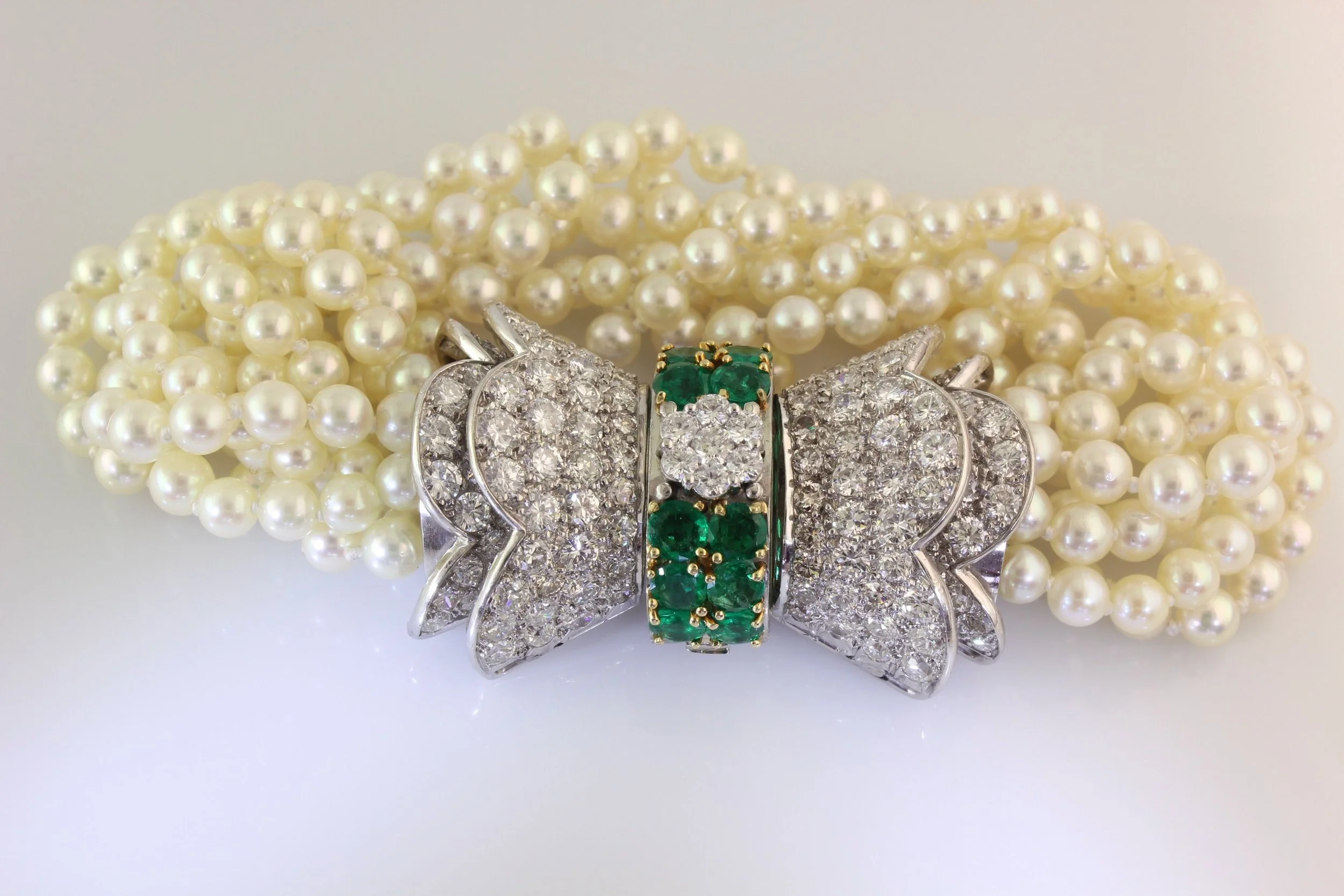 Close-up of a pearl necklace with a large silver and diamond-encrusted butterfly-shaped brooch featuring green gemstones.