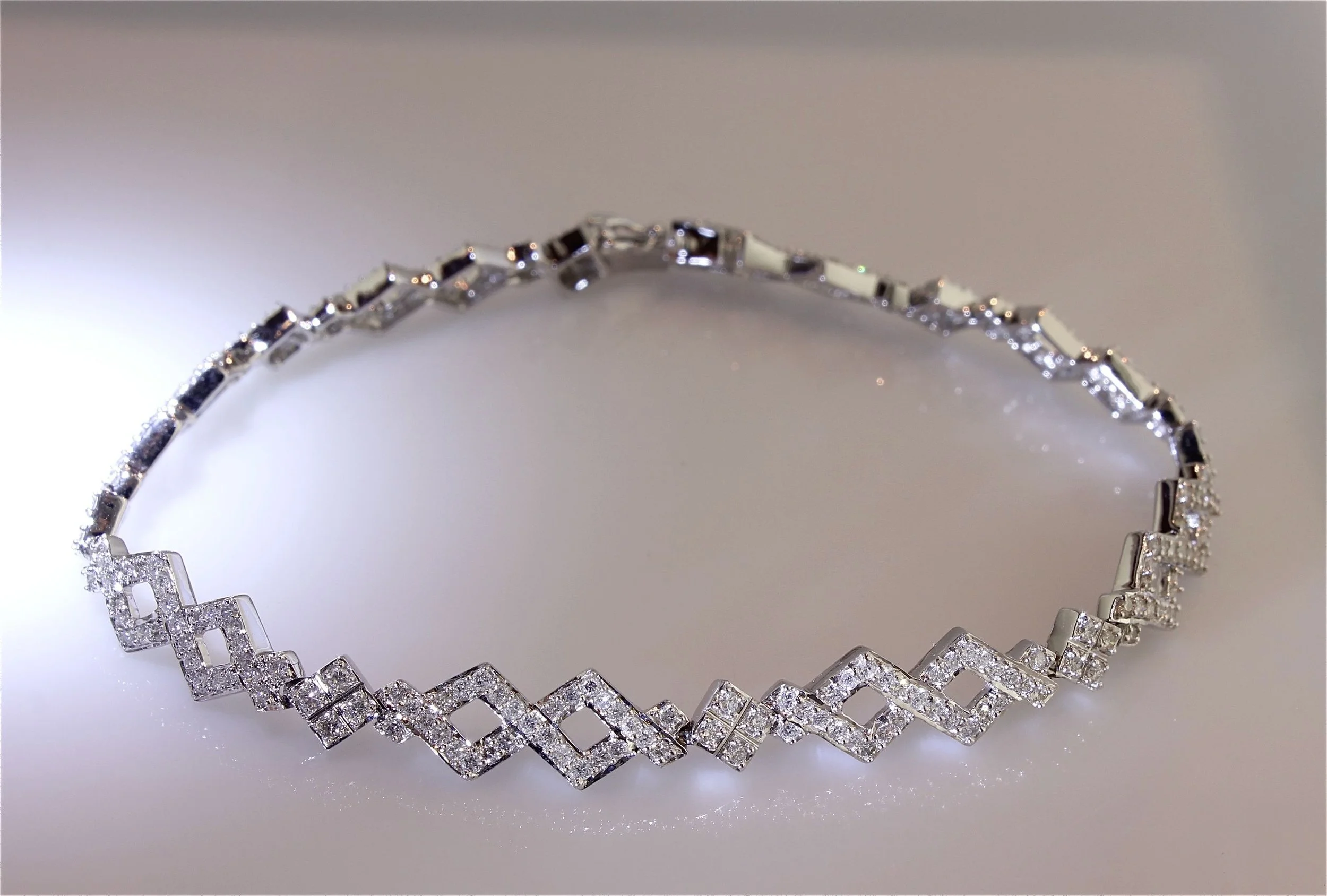 A silver bracelet with square links, each encrusted with small clear stones, on a light background.