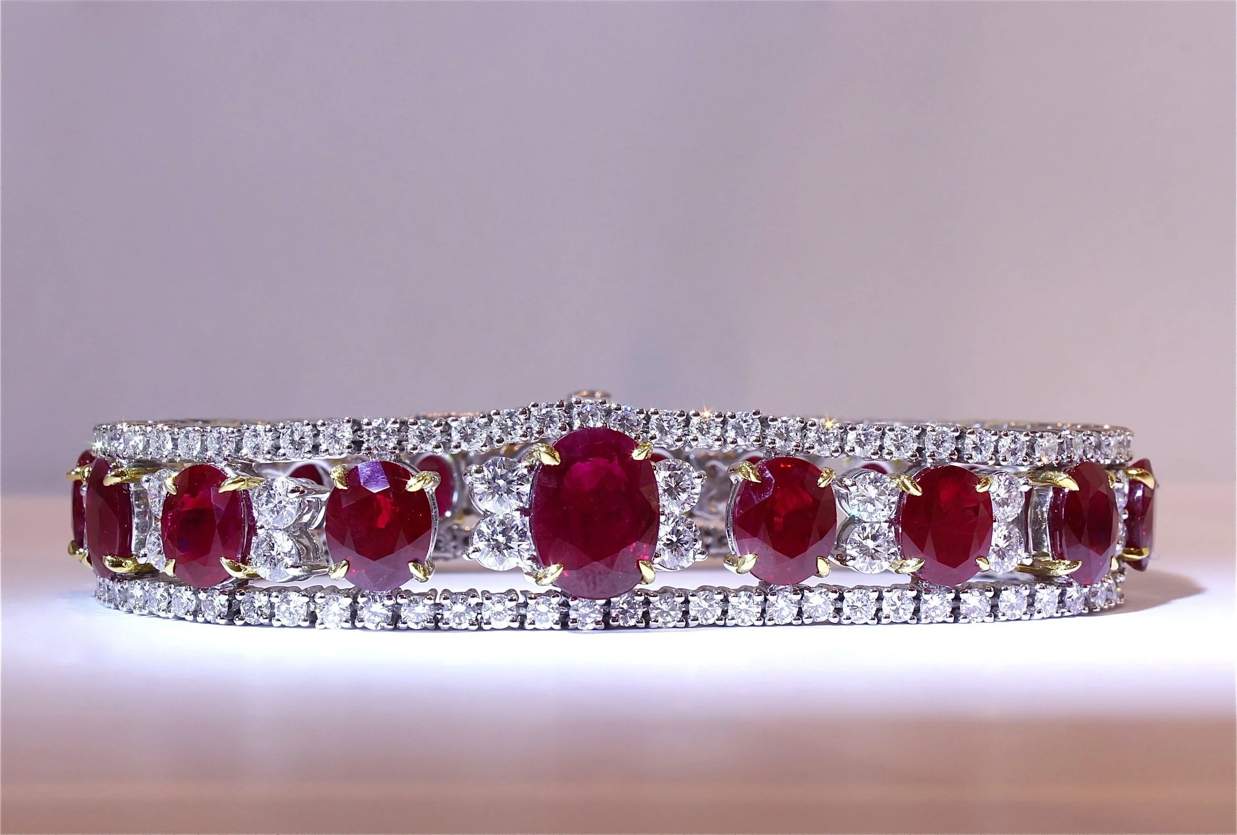 A stack of three diamond and ruby rings, featuring yellow gold bands, with a plain gradient background.
