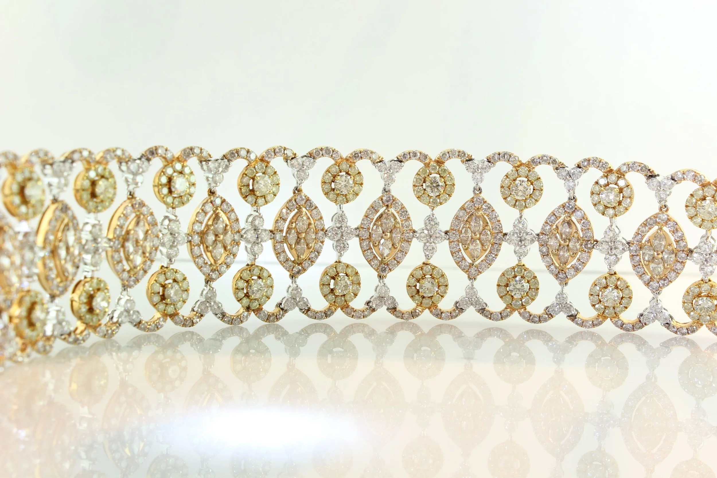 Close-up view of a gold and diamond jewelry bracelet with intricate design, set against a white background.