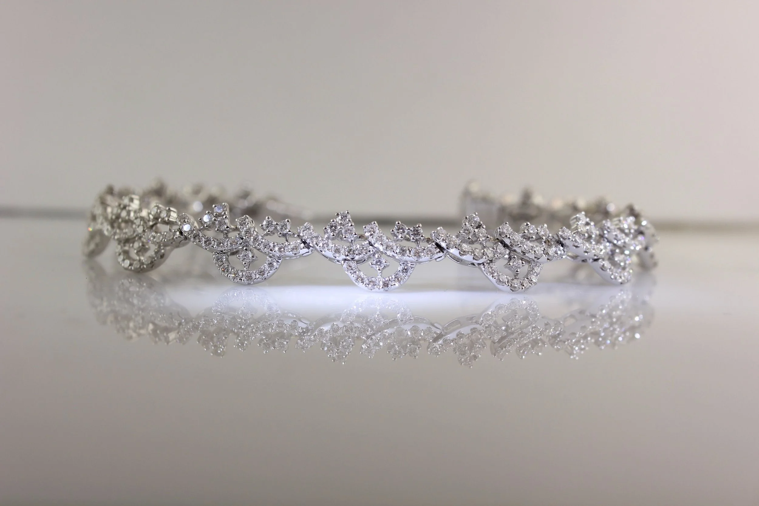 A silver tiara encrusted with numerous sparkling clear gemstones, resting on a reflective surface.