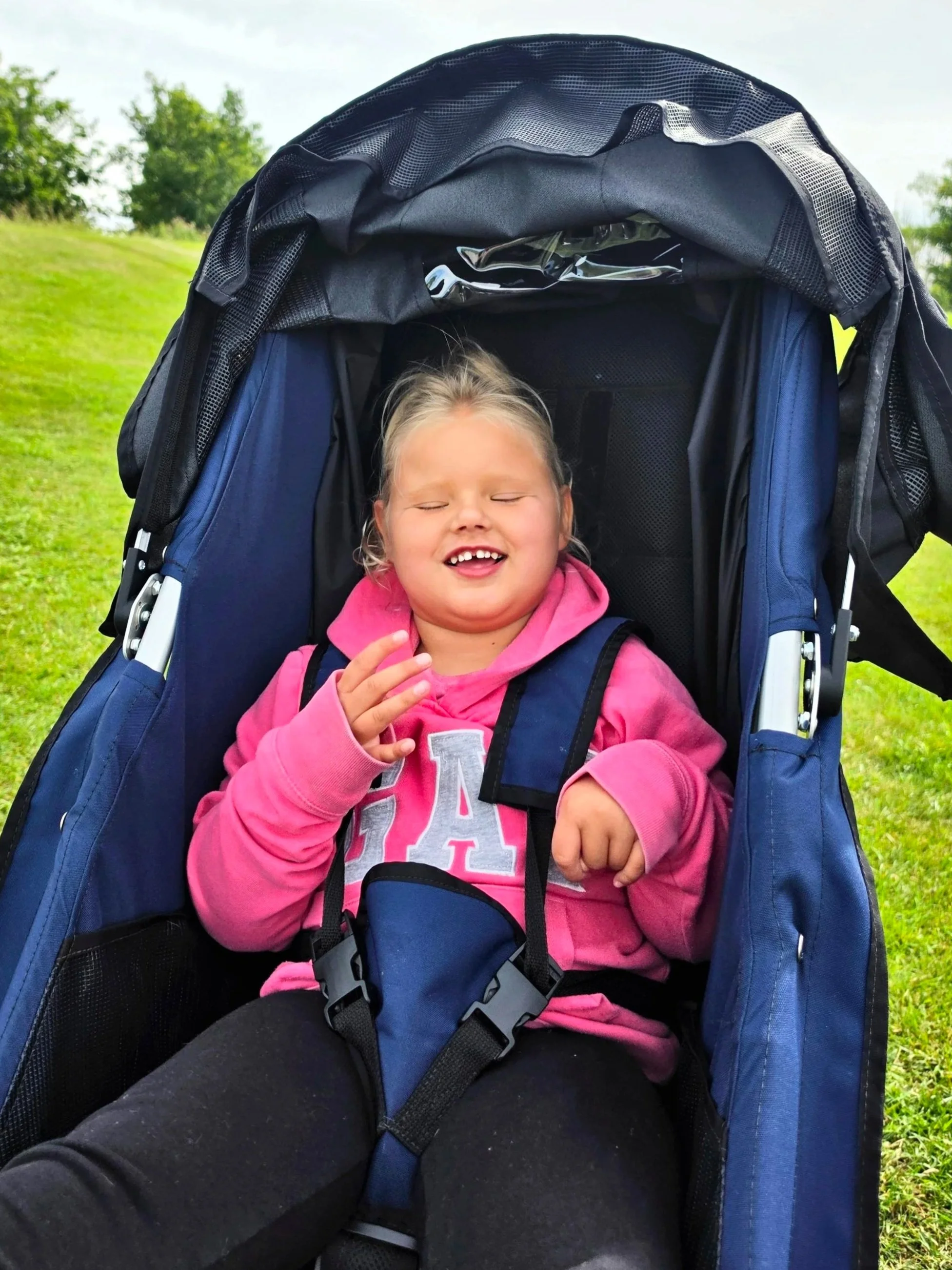 Kira is outside in her pushchair. She has a big smile on her face.