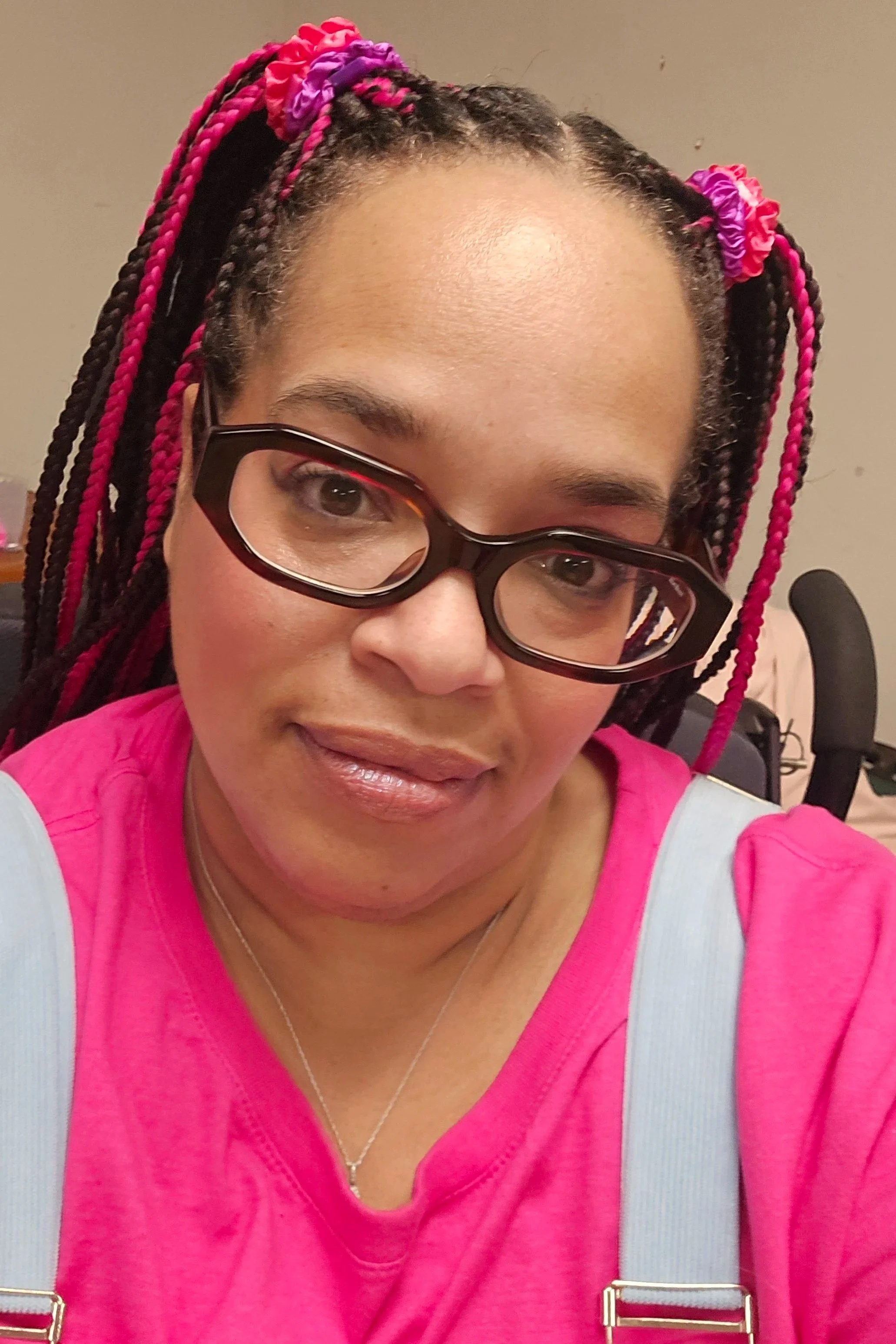 A selfie of Janelle-Marie. She has black and pink braids pulled into pig-tails. She is wearing brown-rimmed glasses and a bright pink shirt.
