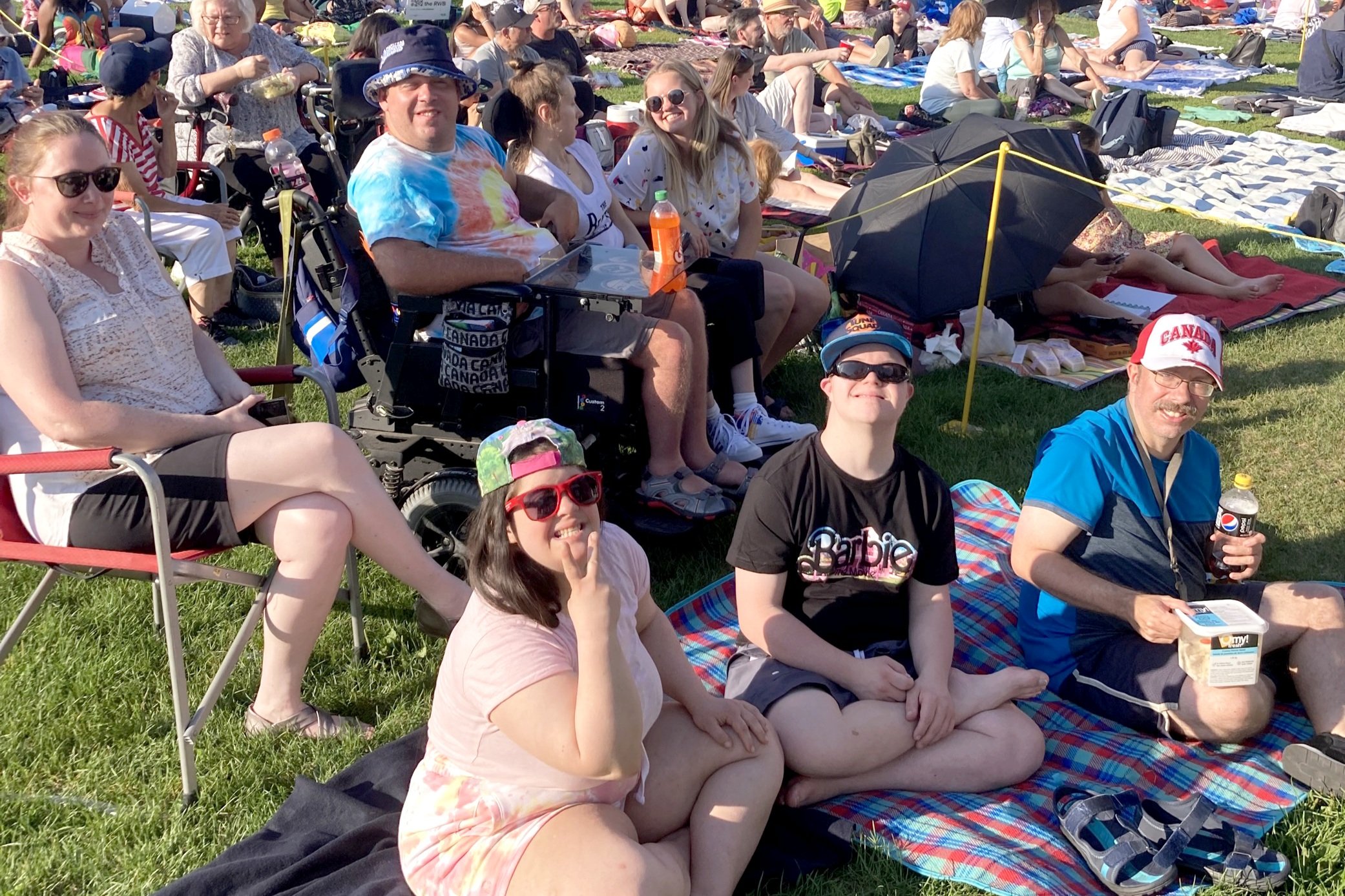 A group of young adults sit on picnic blankets and lawn chairs in a field at Winnipeg Folk Fest.