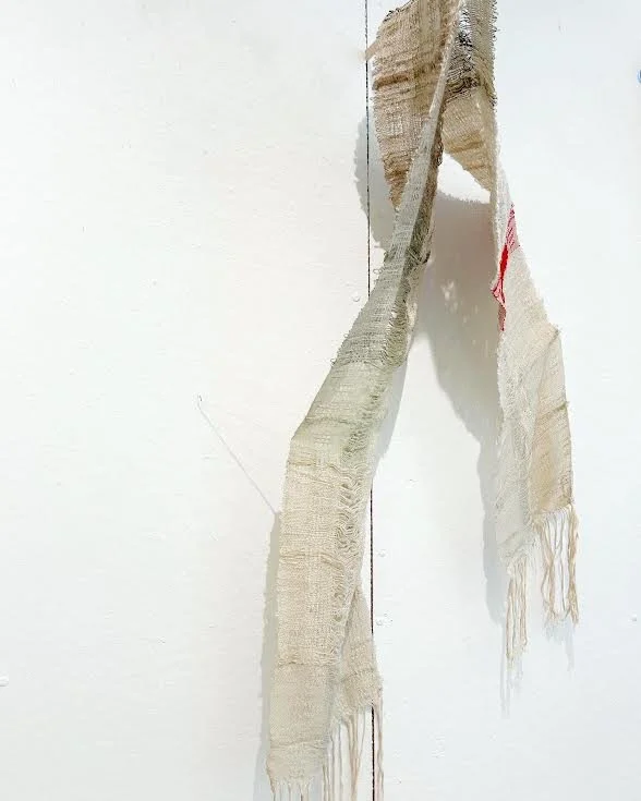 Worn, torn fabric or textile hanging loosely on a plain wall.