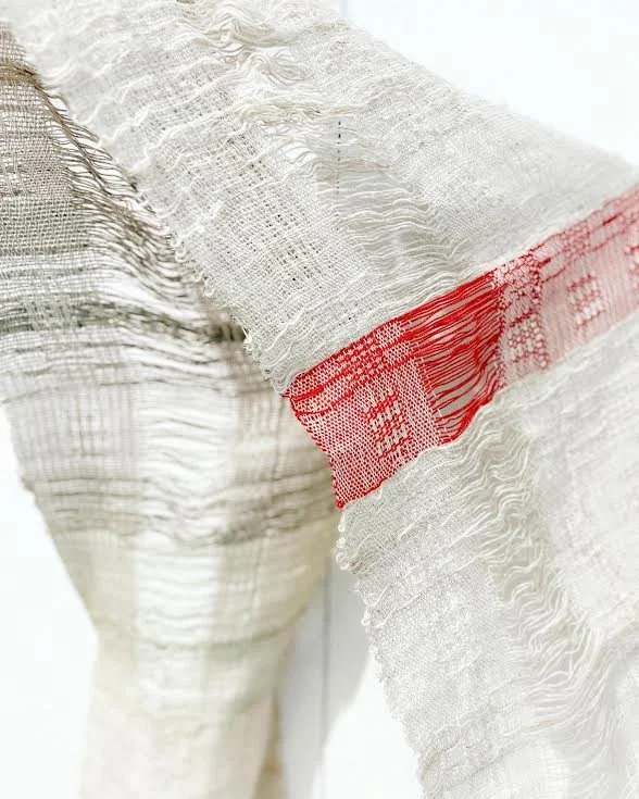 Close-up of a textured fabric with frayed edges and a red horizontal stripe.