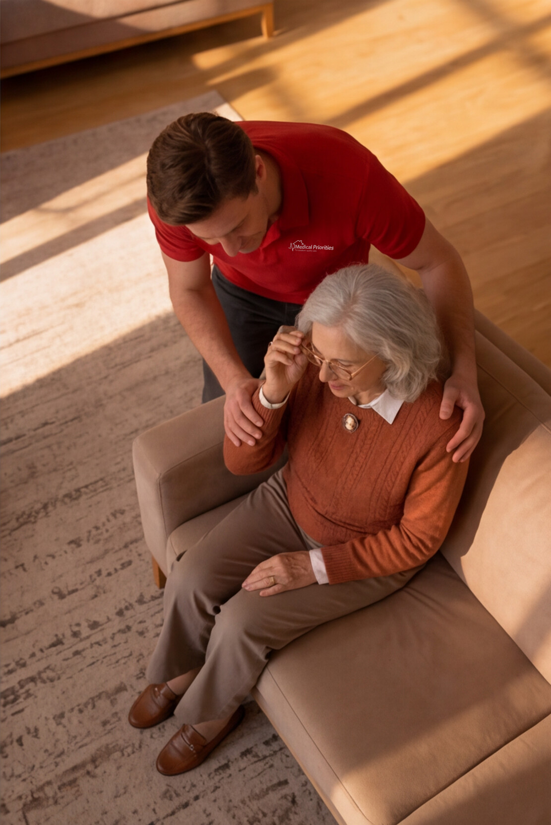 Male caregiver supports a woman sitting on the couch.