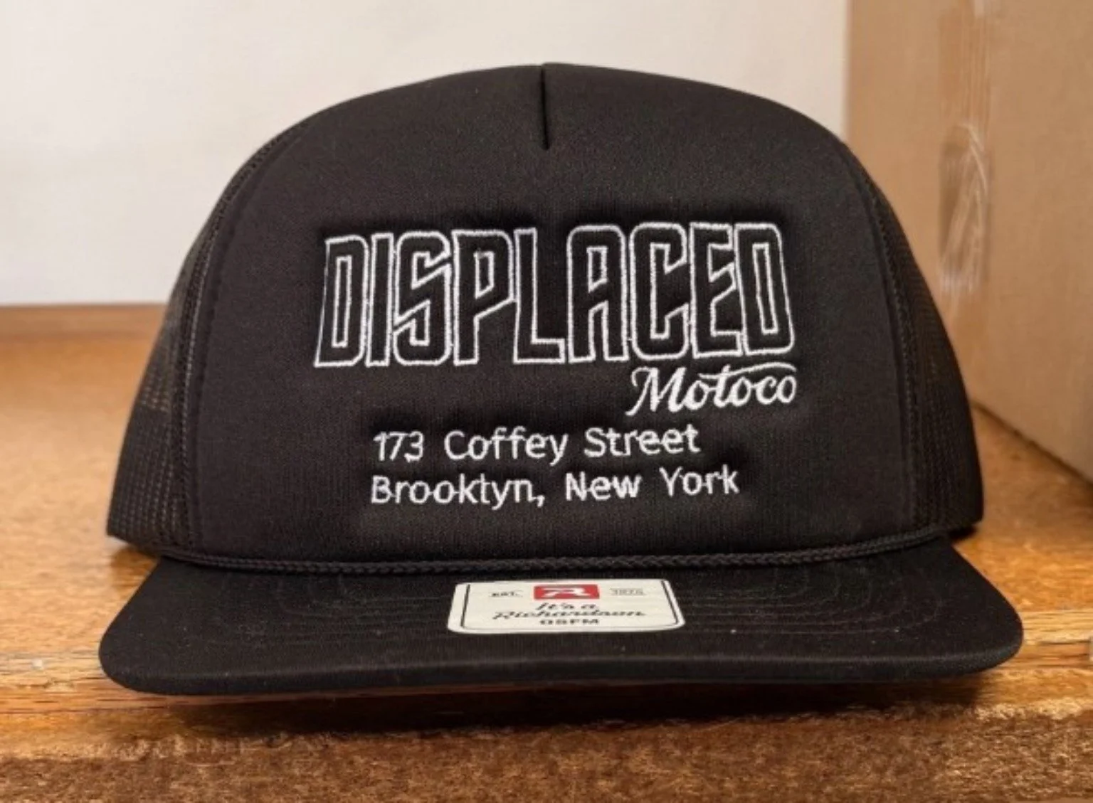 Actual black Displaced Motoco Richardson trucker hat on a wooden counter