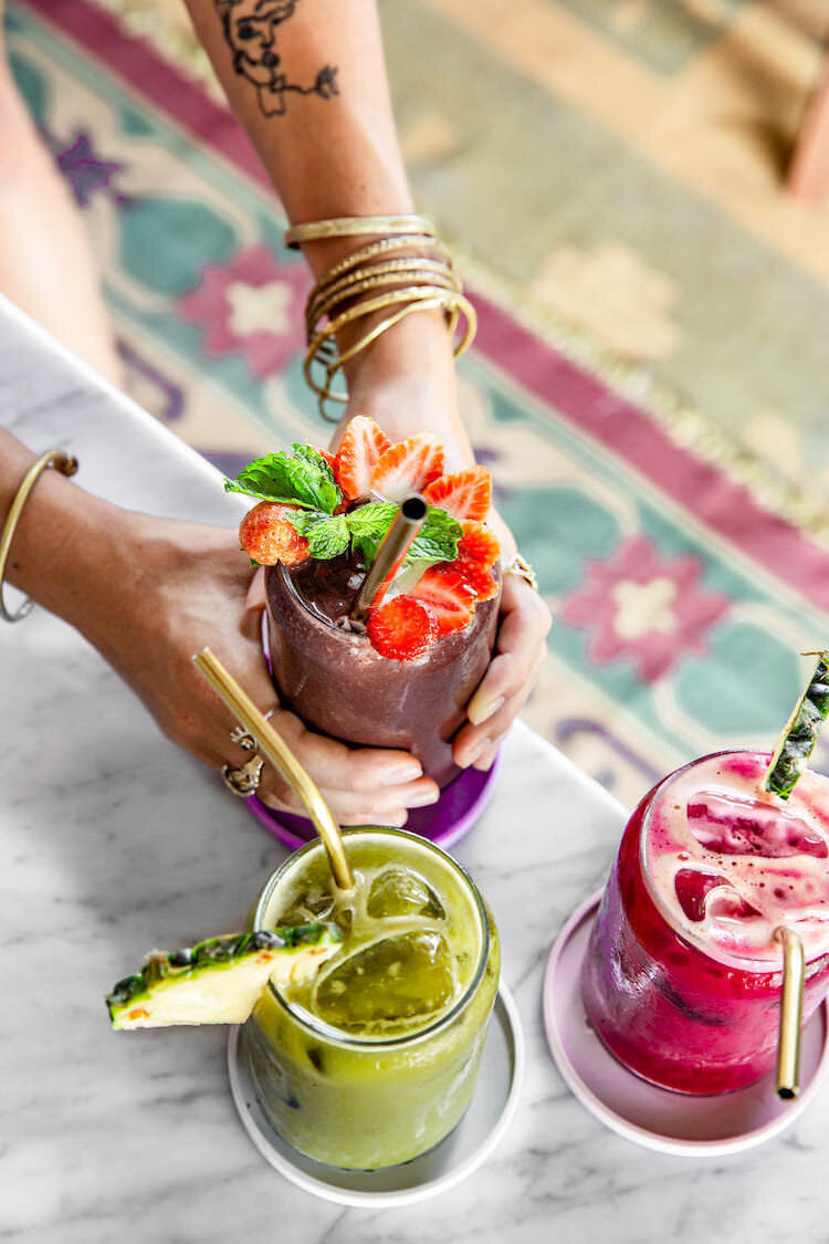 Three colorful beverages with fruit garnishes on a marble table, with a patterned rug in the background in Canggu, Bali.