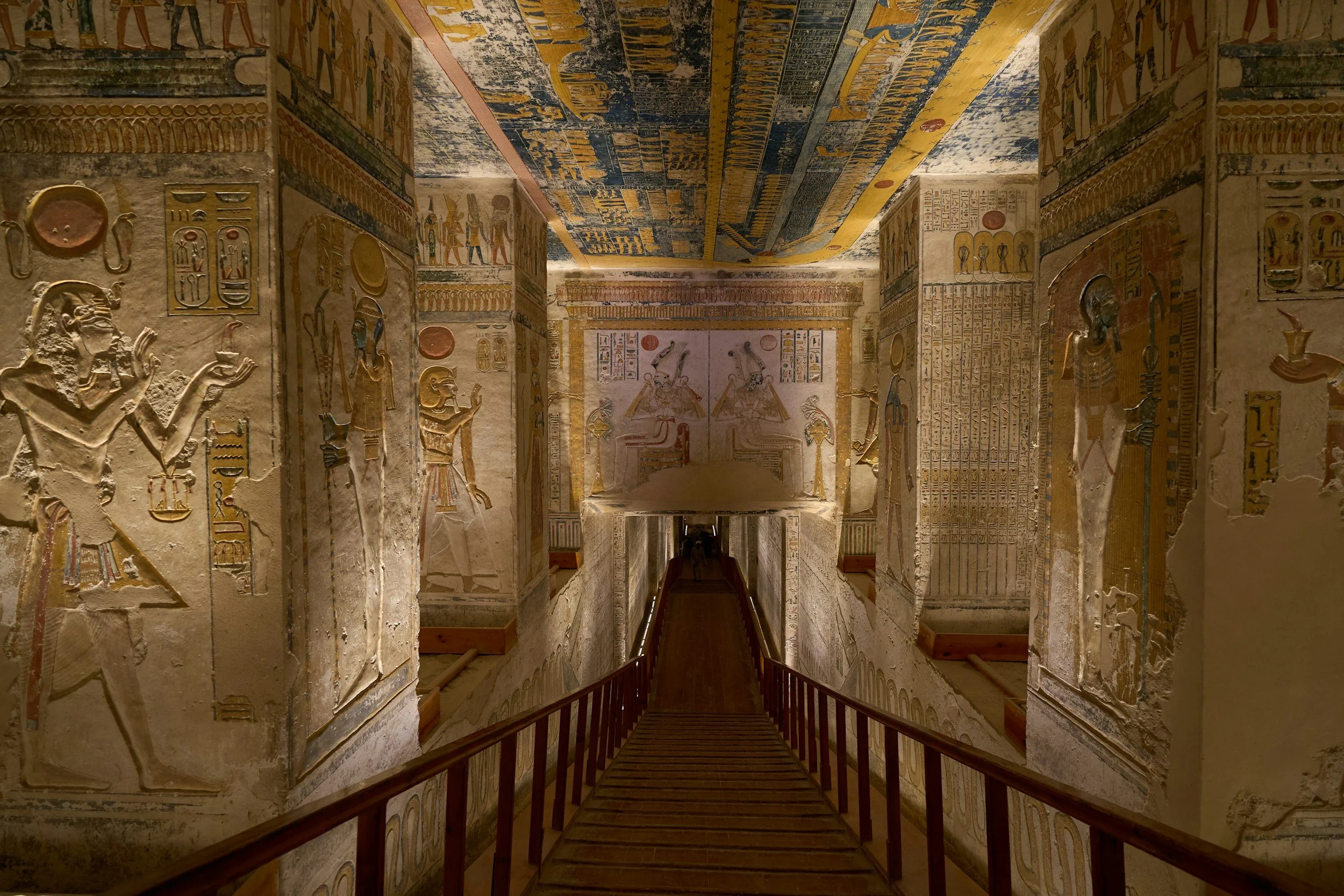Interior of an ancient Egyptian tomb decorated with colorful hieroglyphics and relief carvings of Egyptian gods and figures.
