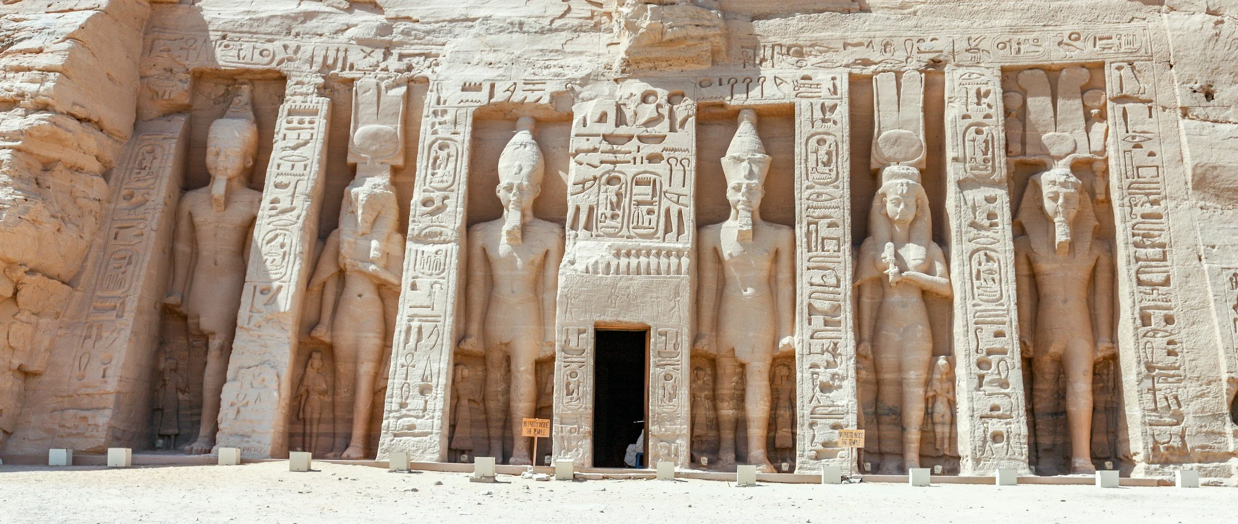 Ancient Egyptian temple with carved statues of Egyptian gods and hieroglyphic inscriptions on the stone façade.