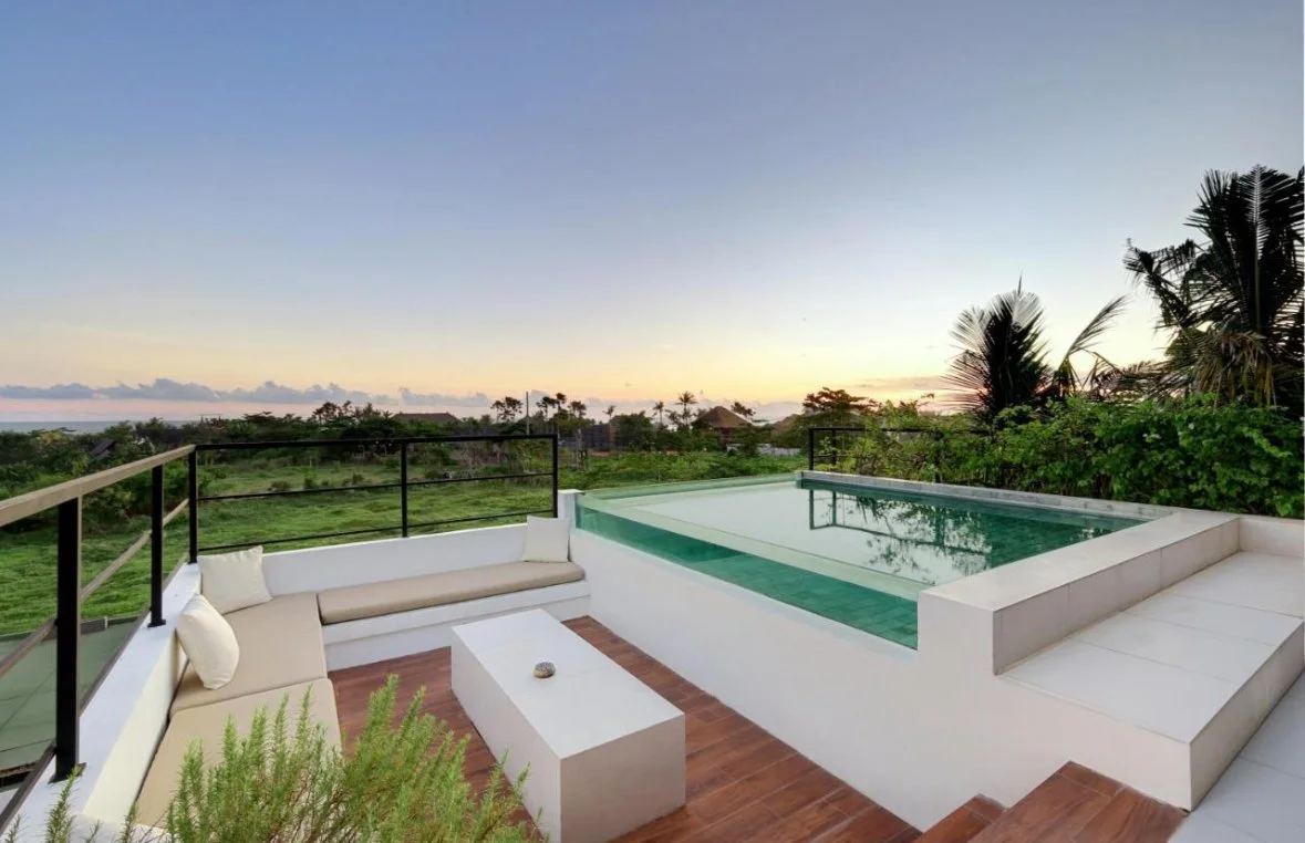 A rooftop pool with a seating area and scenic view of trees and the horizon at sunset.