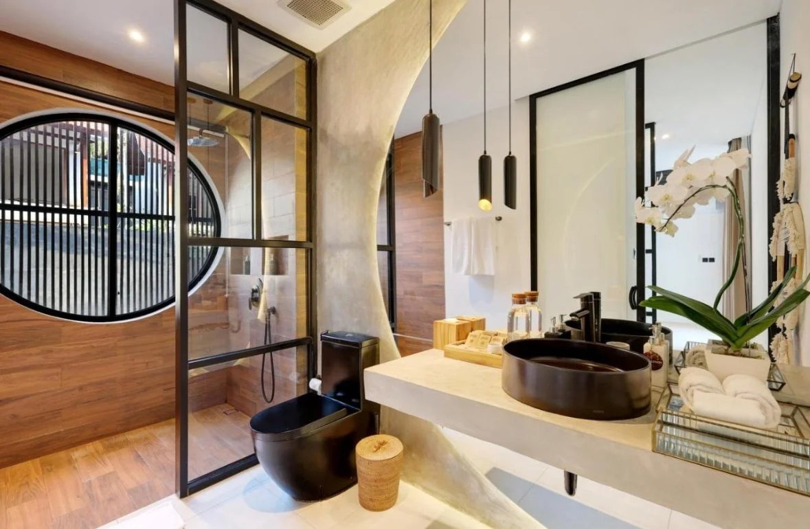 Modern bathroom with black toilet, black sink, wooden accents, glass partition, and decorative items including a white orchid
