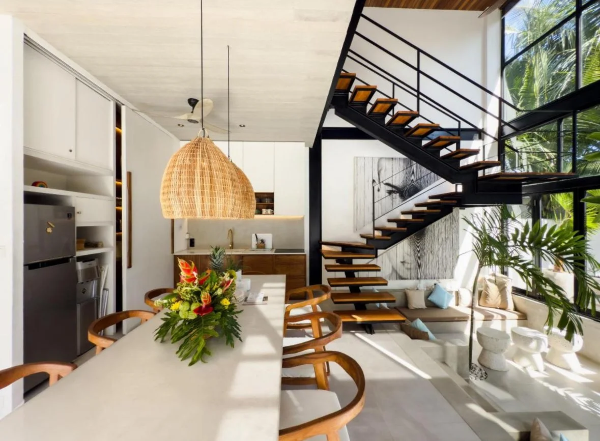 Open-concept kitchen and living area with a staircase, large windows, and greenery outside