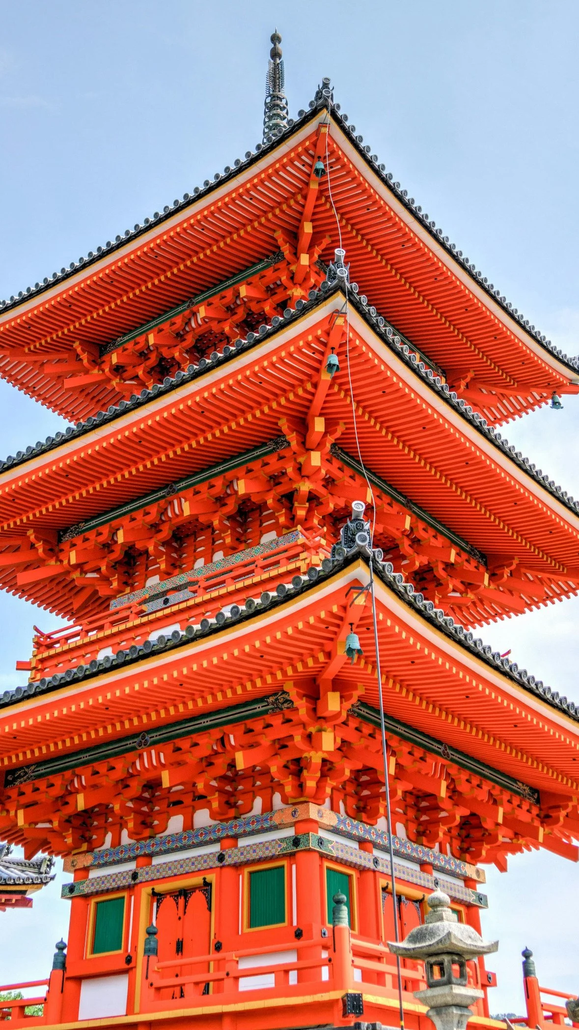 A traditional multi-tiered Japanese pagoda in Tokyo with orange and red colors, intricate wooden details, and a stone lantern in the foreground against a blue sky.