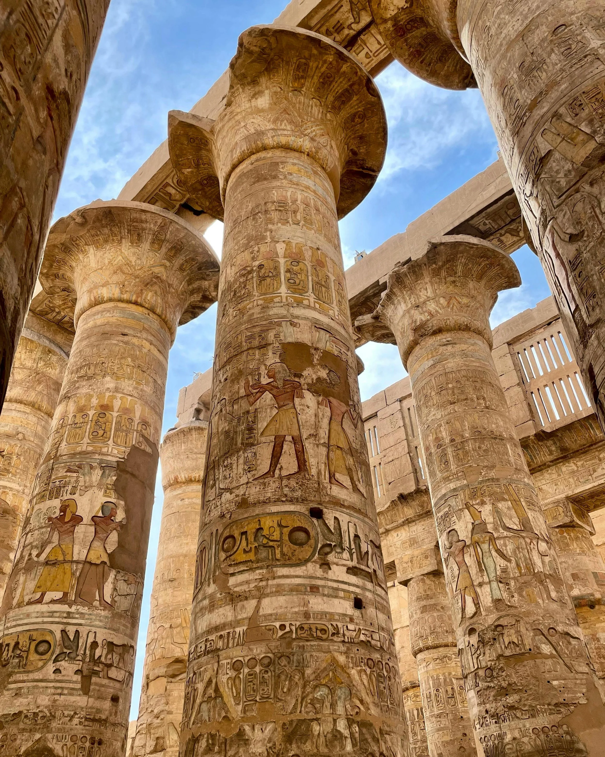 Ancient Egyptian temple columns decorated with hieroglyphics and carvings of gods and pharaohs, under a blue sky.