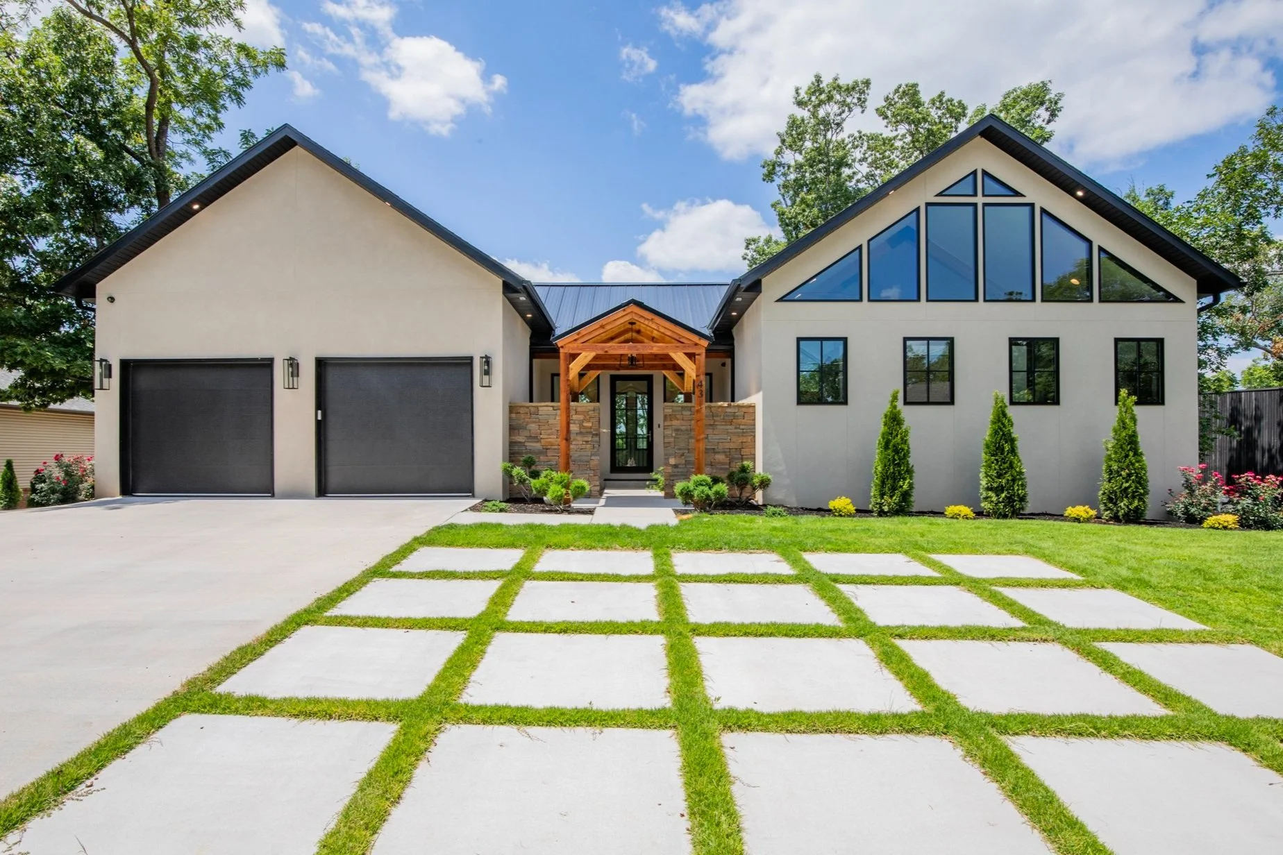 Modern house with a front yard featuring a sparkling concrete pathway separated by grass and a green lawn, trees, and a blue sky background.