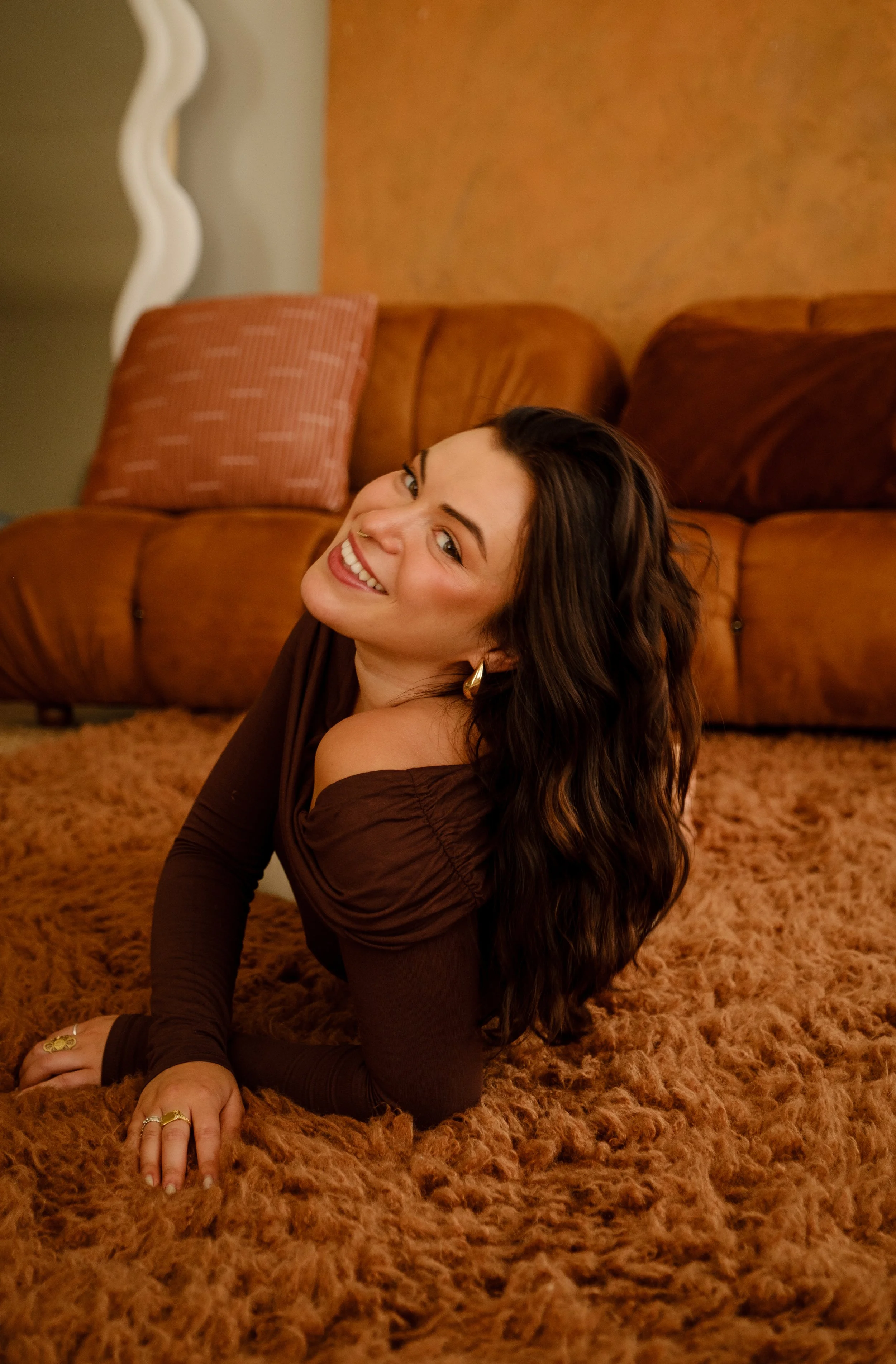A photo of Claire laying on a brown rug on her side with her head tilted to the side and smiling