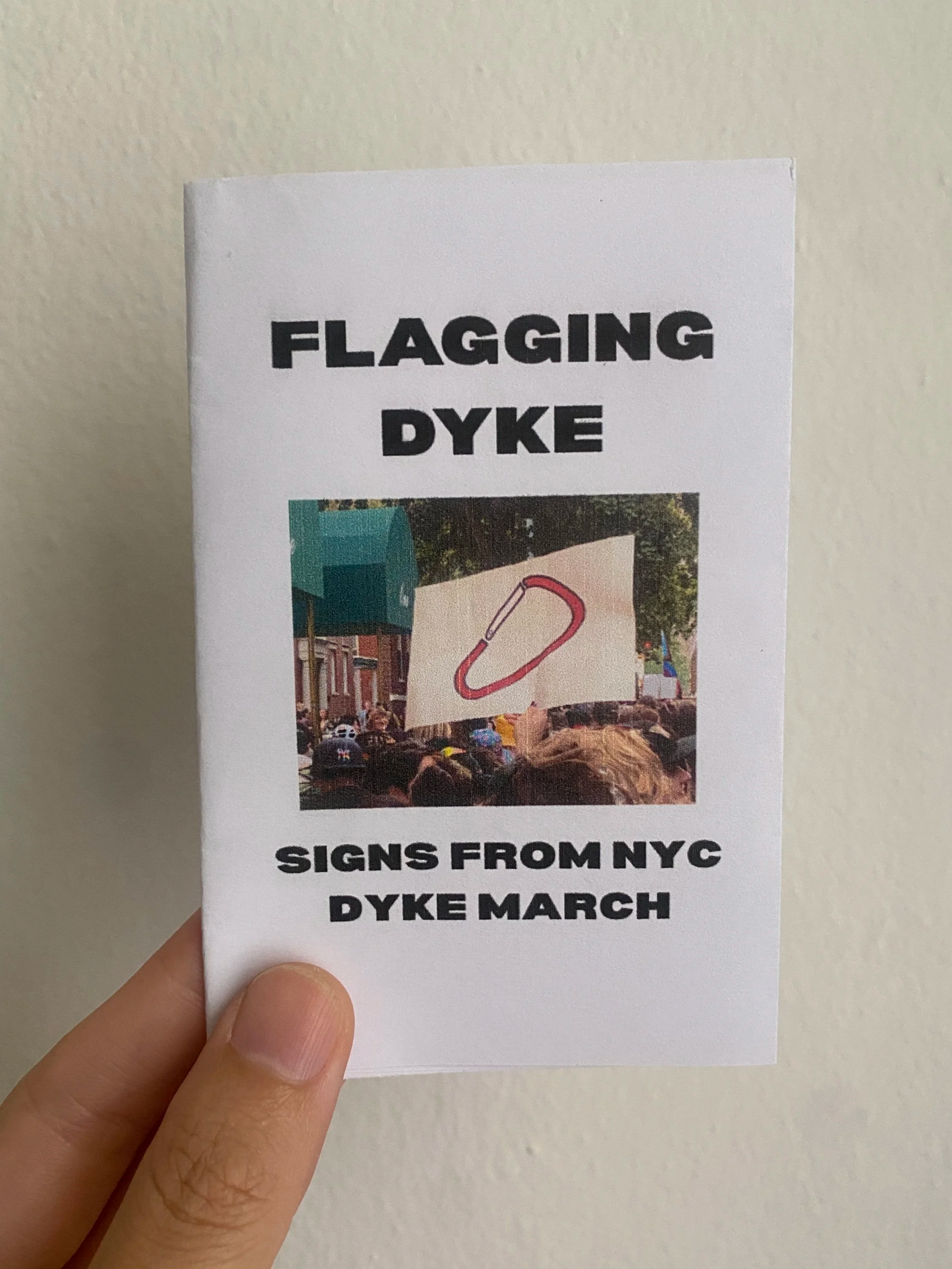Flagging Dyke: Signs from NYC Dyke March; Image of a poster with an illustration of a red carabiner being held over a crowd.