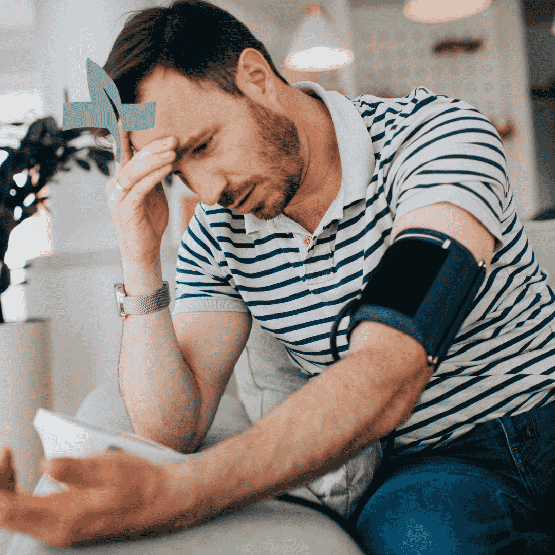 A man holding his head while checking his blood pressure at home, highlighting symptoms of hypotension.