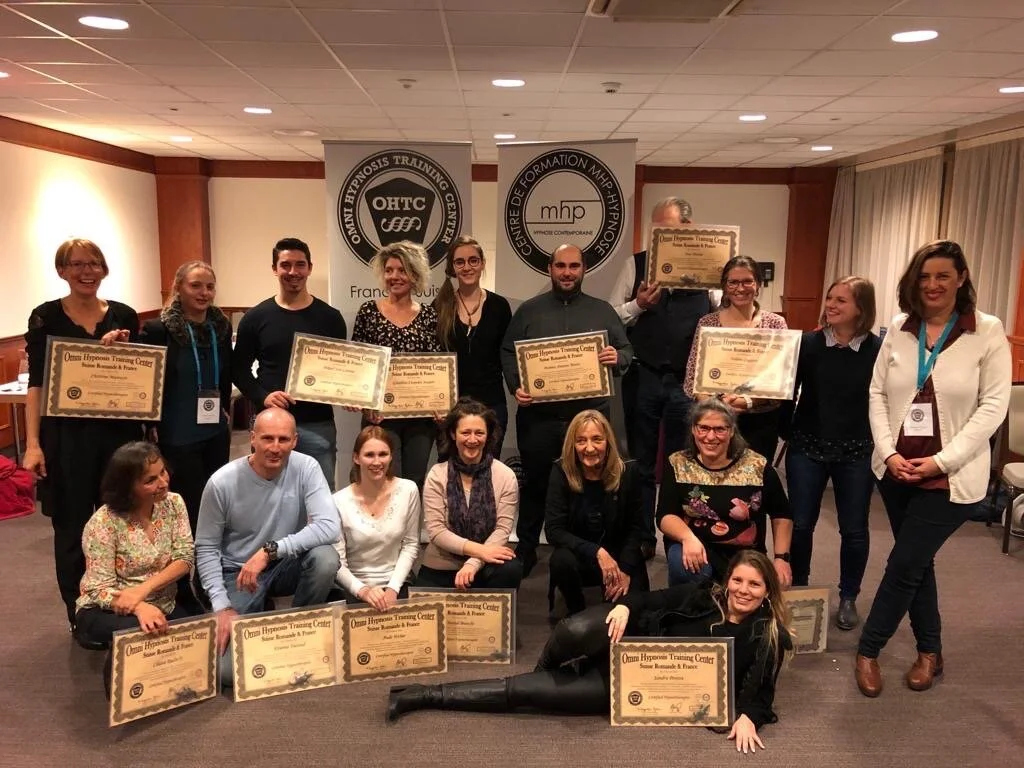 Groupe de personnes posant lors d'une cérémonie de remise de diplômes ou certificats, plusieurs retenant leurs diplômes, dans une salle de formation.