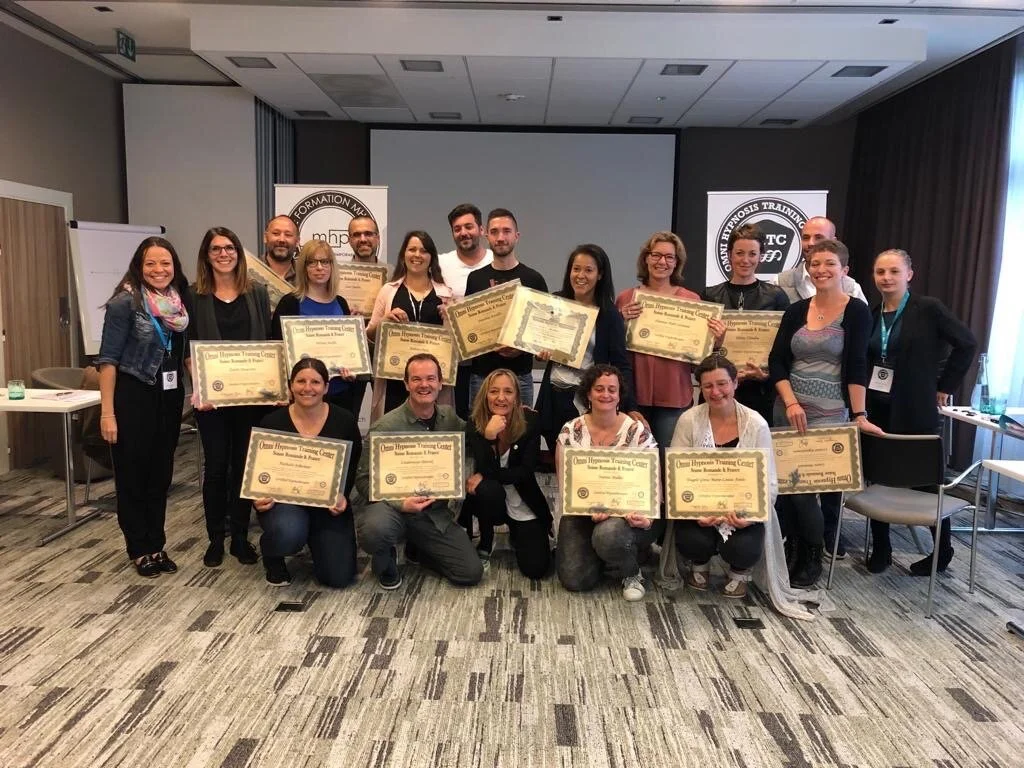 Groupe de personnes posant avec des certificats lors d'une formation ou d'une cérémonie de remise de diplômes dans une salle de conférence.