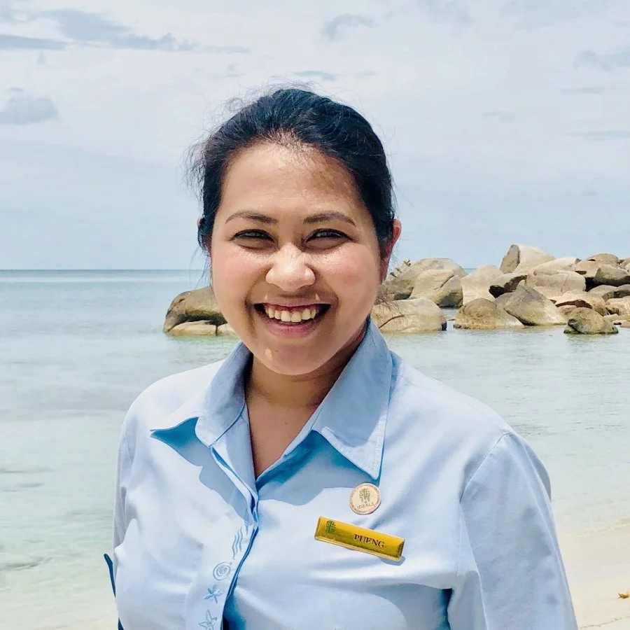 Woman smiling on a beach with rocks in the background.