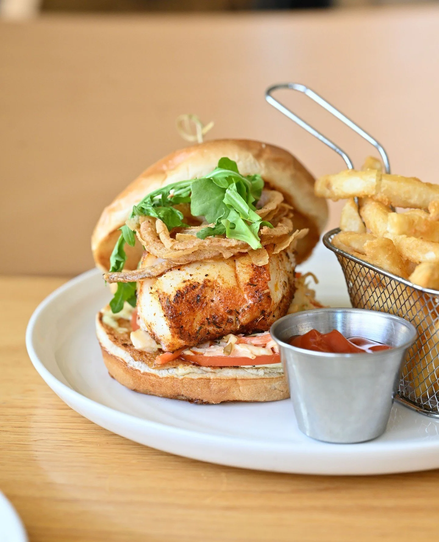 Cajun spice meets New England freshness! Our Blackened Cod Sandwich layers Cajun-seasoned cod with slaw, tomato, arugula, tartar, and crispy onion rings -  best enjoyed with a side of fries and a view of Wellesley Square. 🍽️ #CottageWellesley