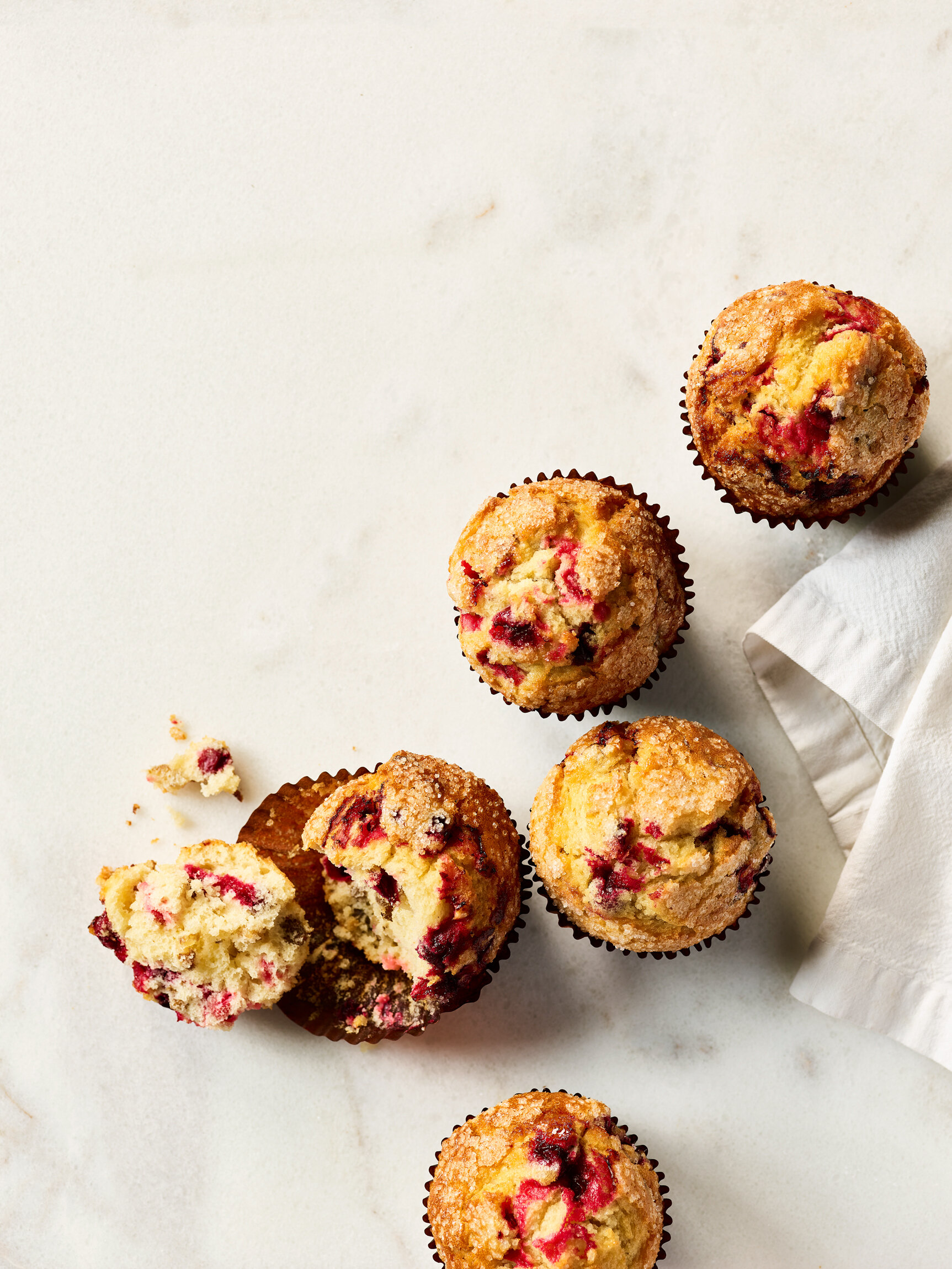 Seven blueberry muffins on a white surface, with one partially broken open and a white napkin nearby. Photographed for Au Bon Pain Cafe. Boston based food and hospitality photographer.